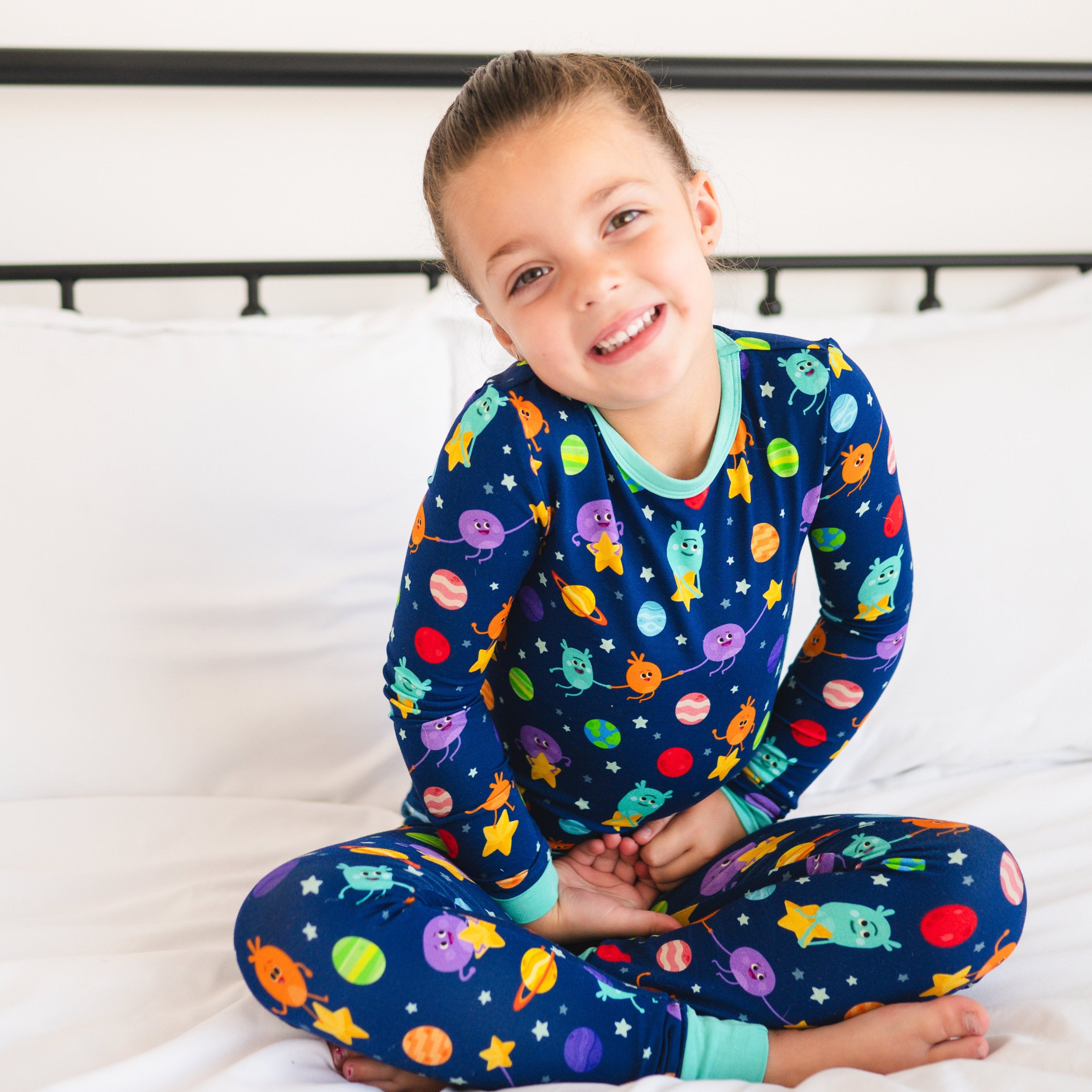 A young girl smiles while wearing blue pajamas with a space-themed print.