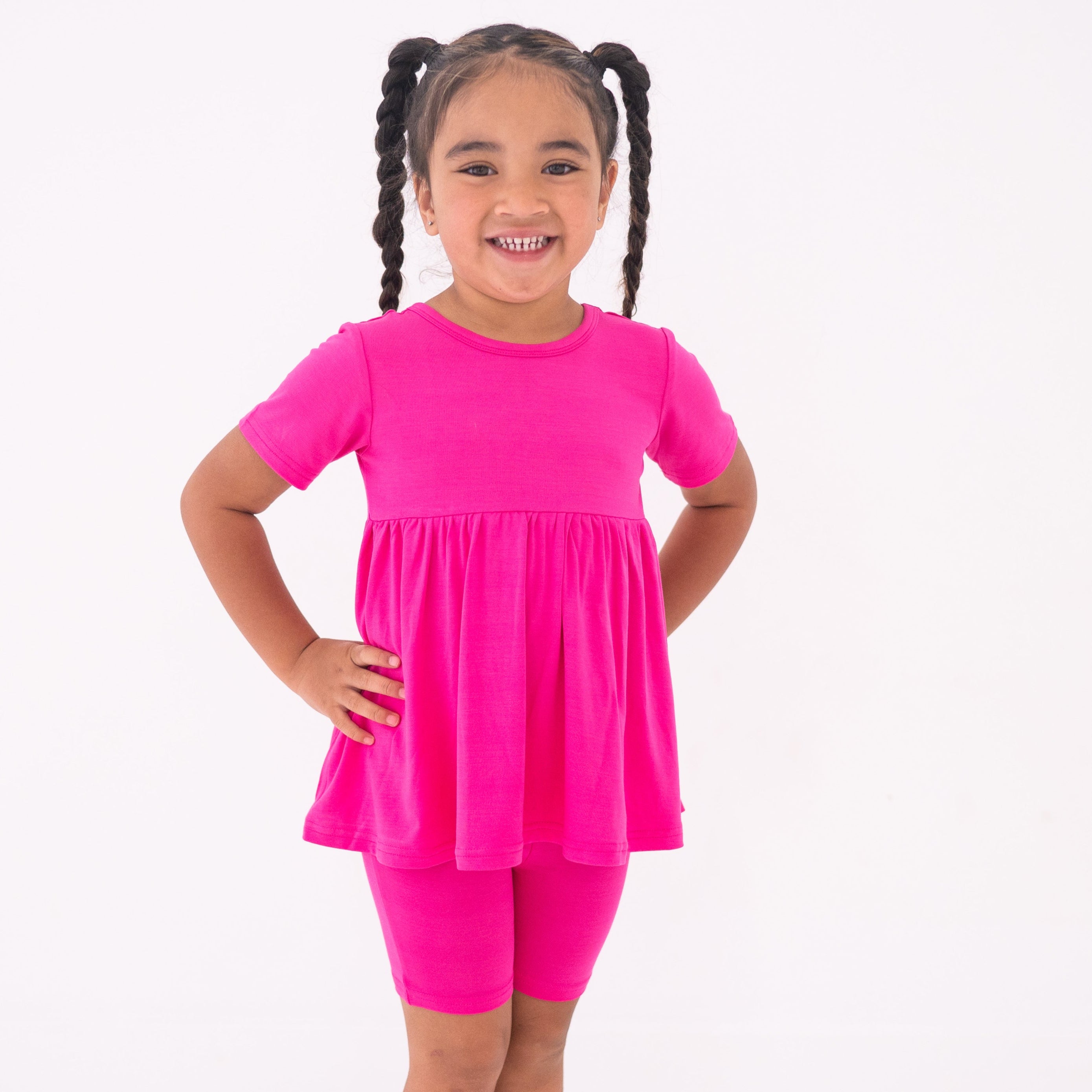 Young girl smiling in a pink peplum top and shorts made of luxe bamboo.