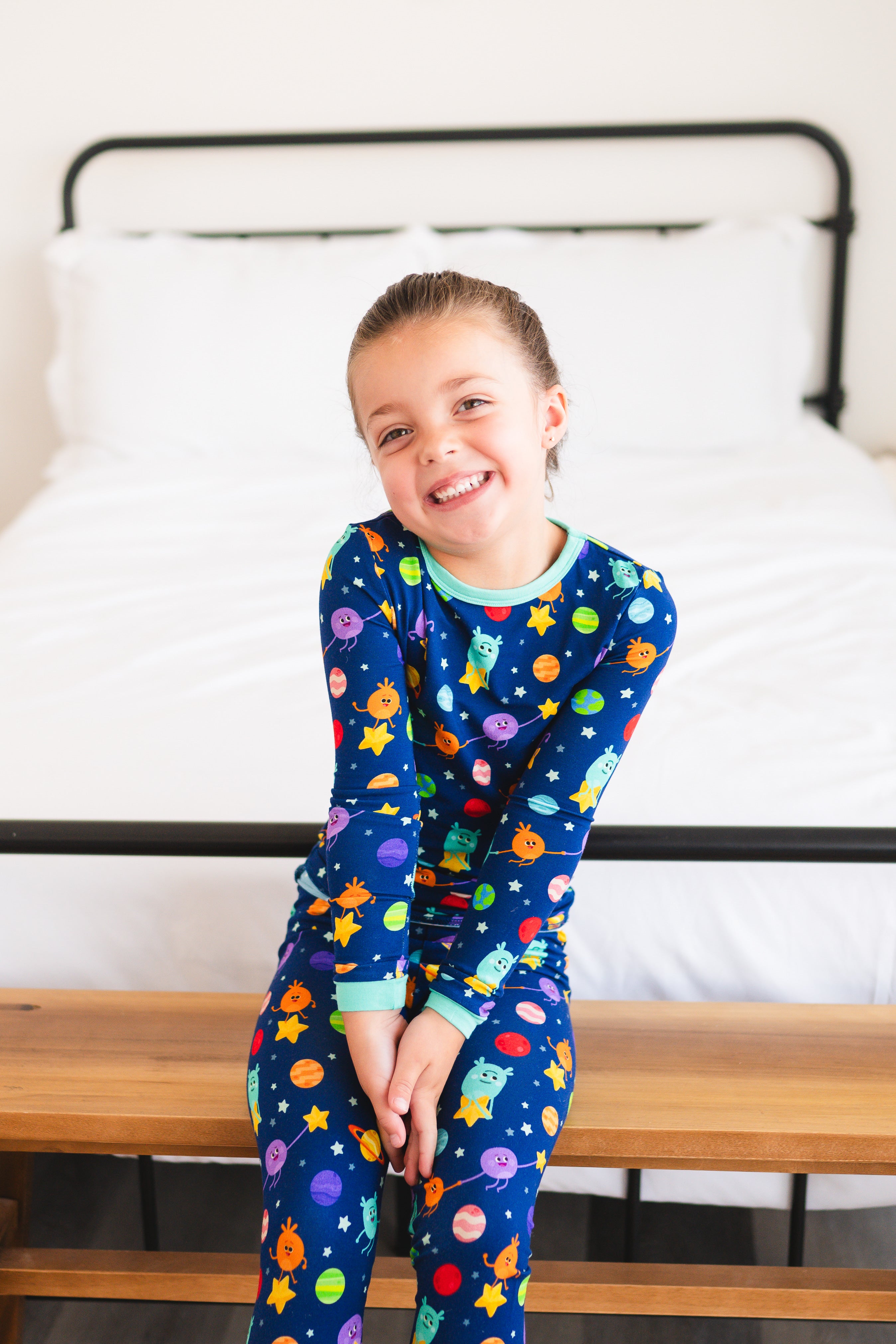 A young girl smiles in blue pajamas with a space-themed print.