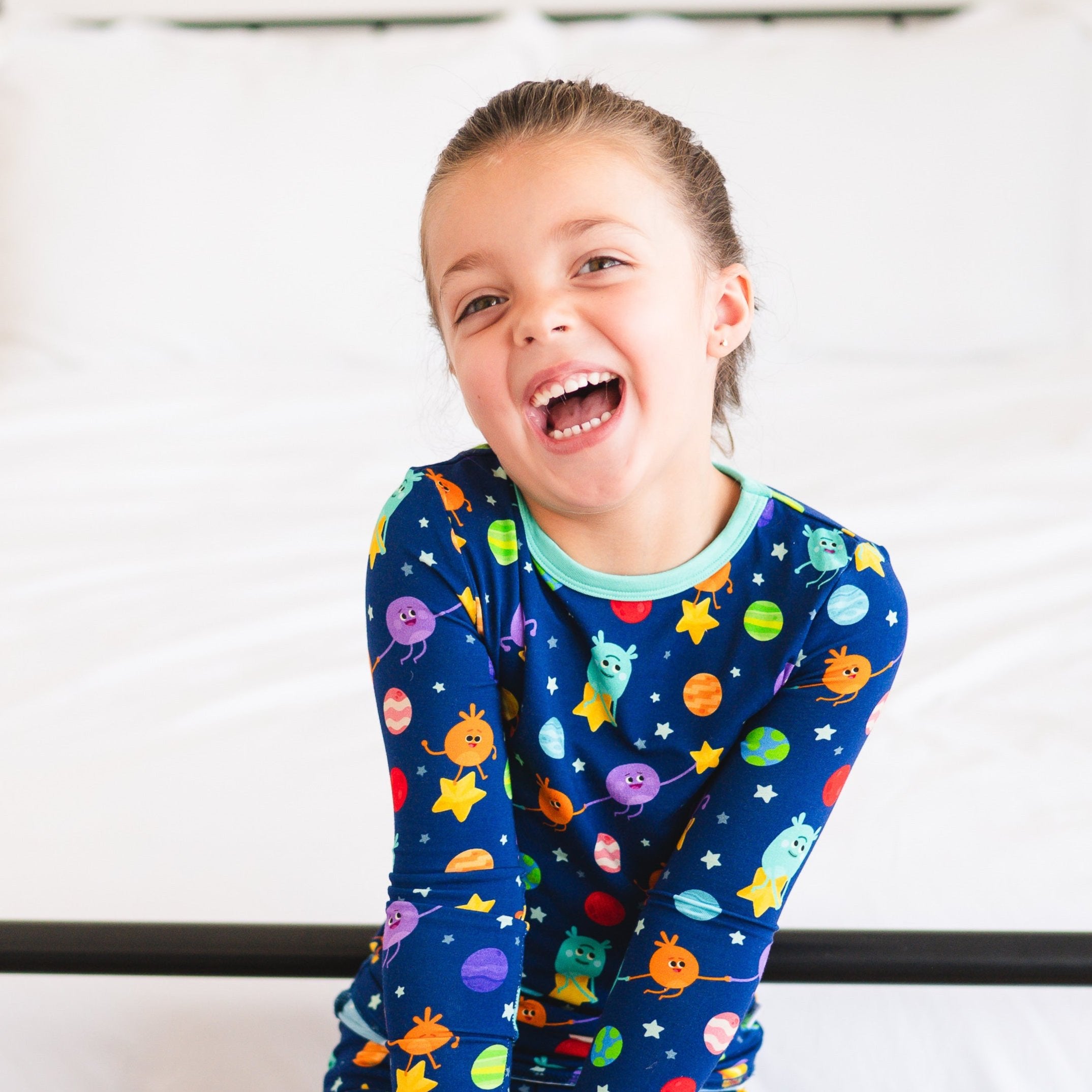 A young girl laughs in blue pajamas with a space-themed Bumble Nums print.