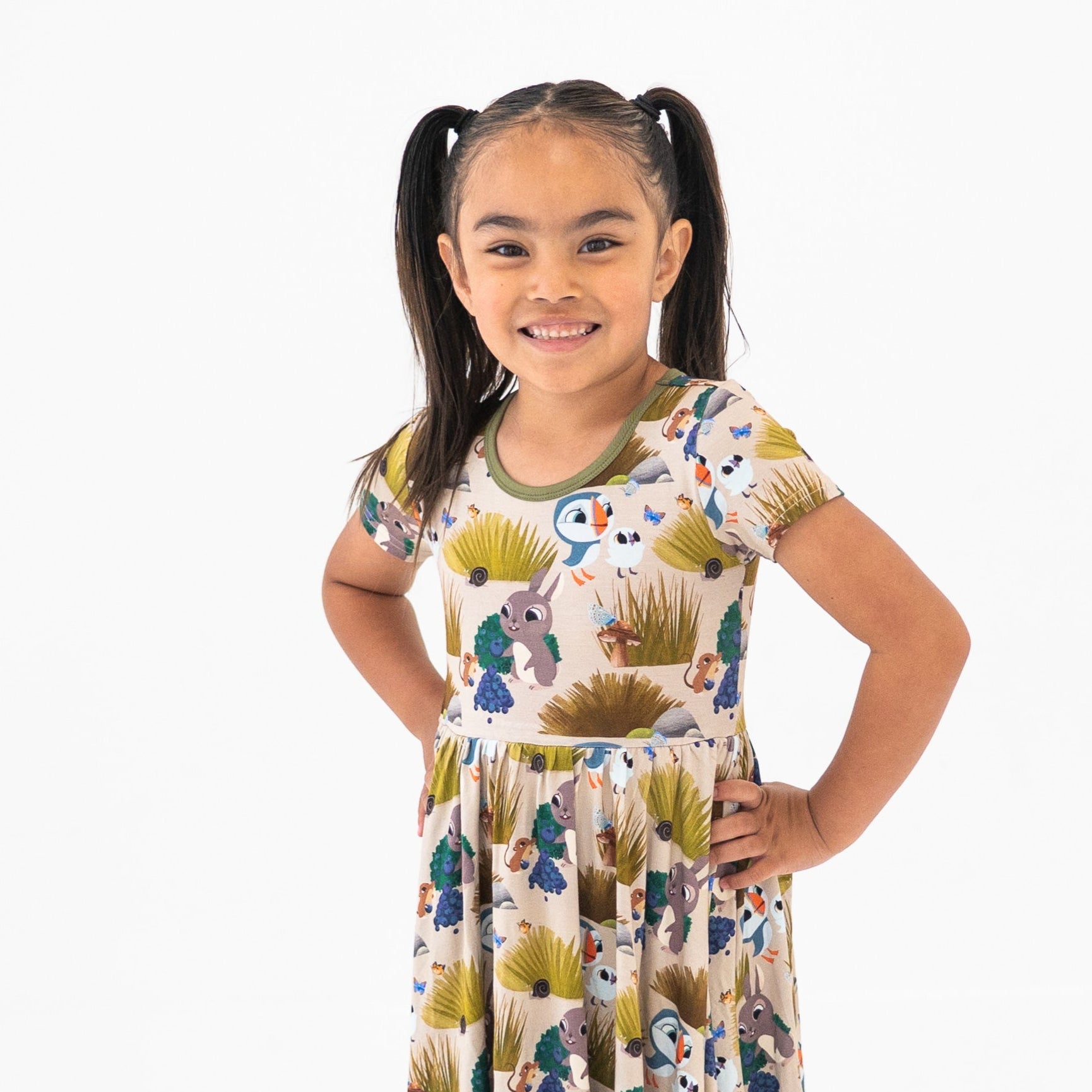 A young girl with pigtails wears a tan dress with a Puffin Rock print.