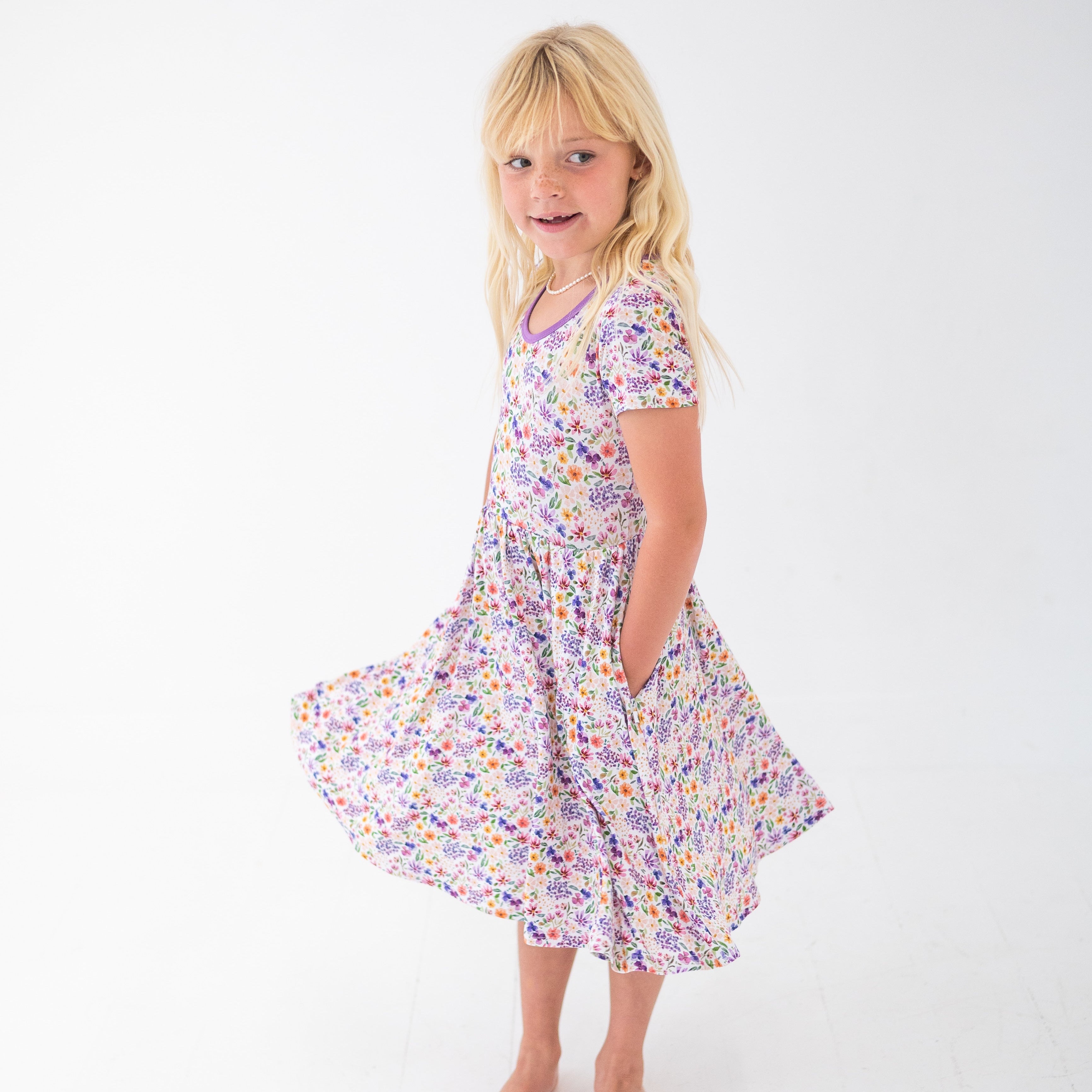 A young girl in a white dress with a floral print and purple trim.