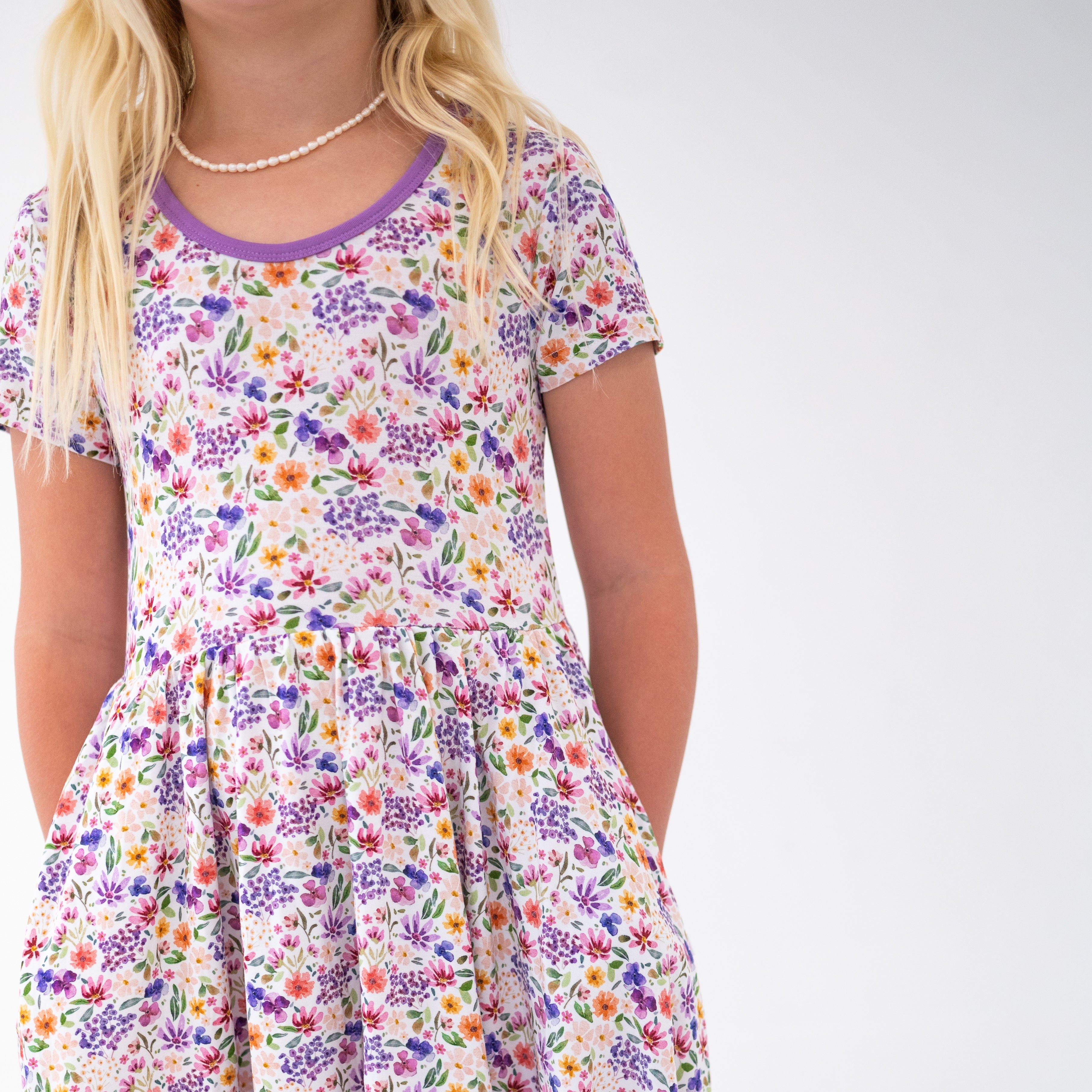 A girl wears a white dress with a floral print and a purple neckline.