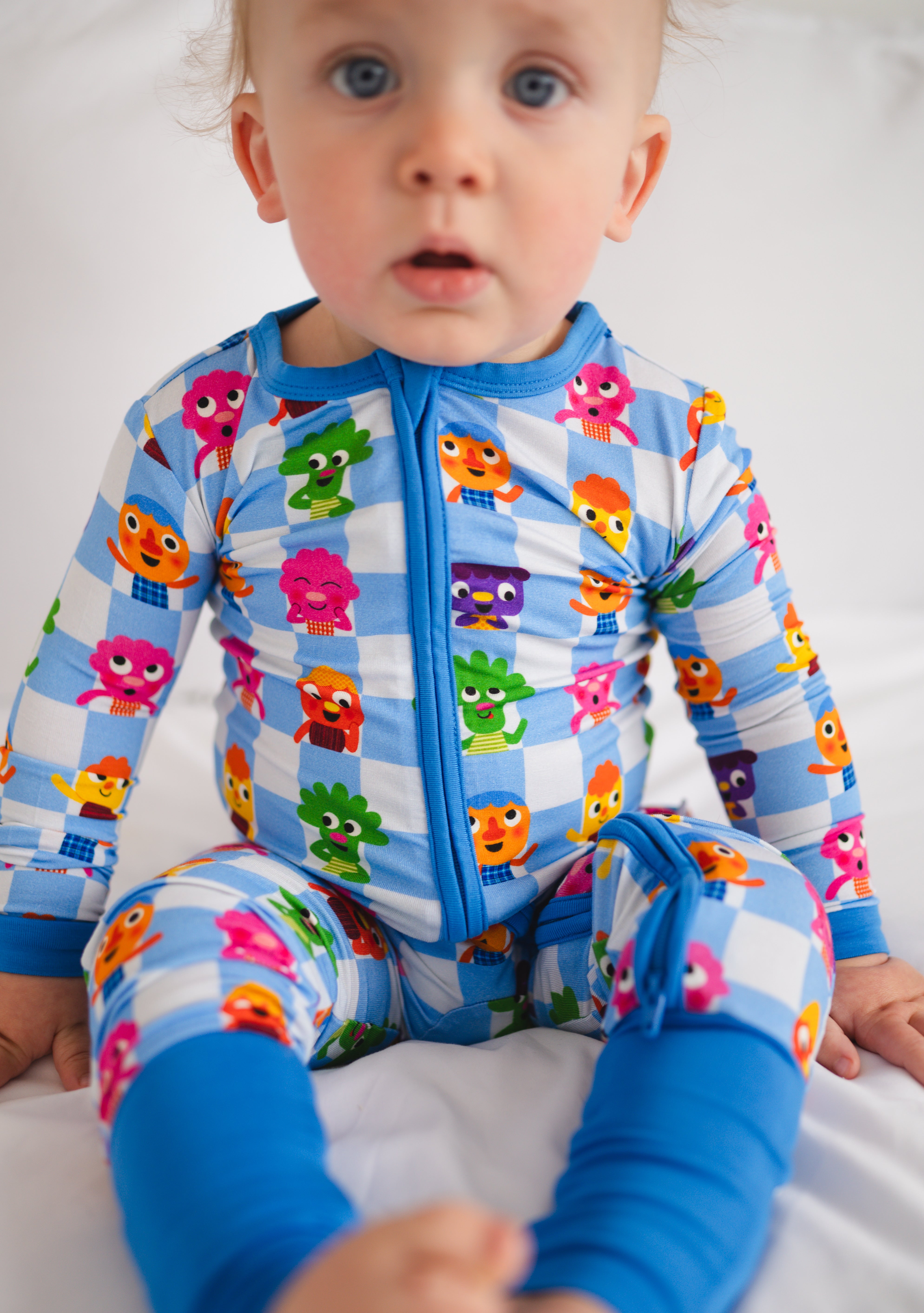 A baby wearing a blue and white checkered pajama set with colorful monster characters.