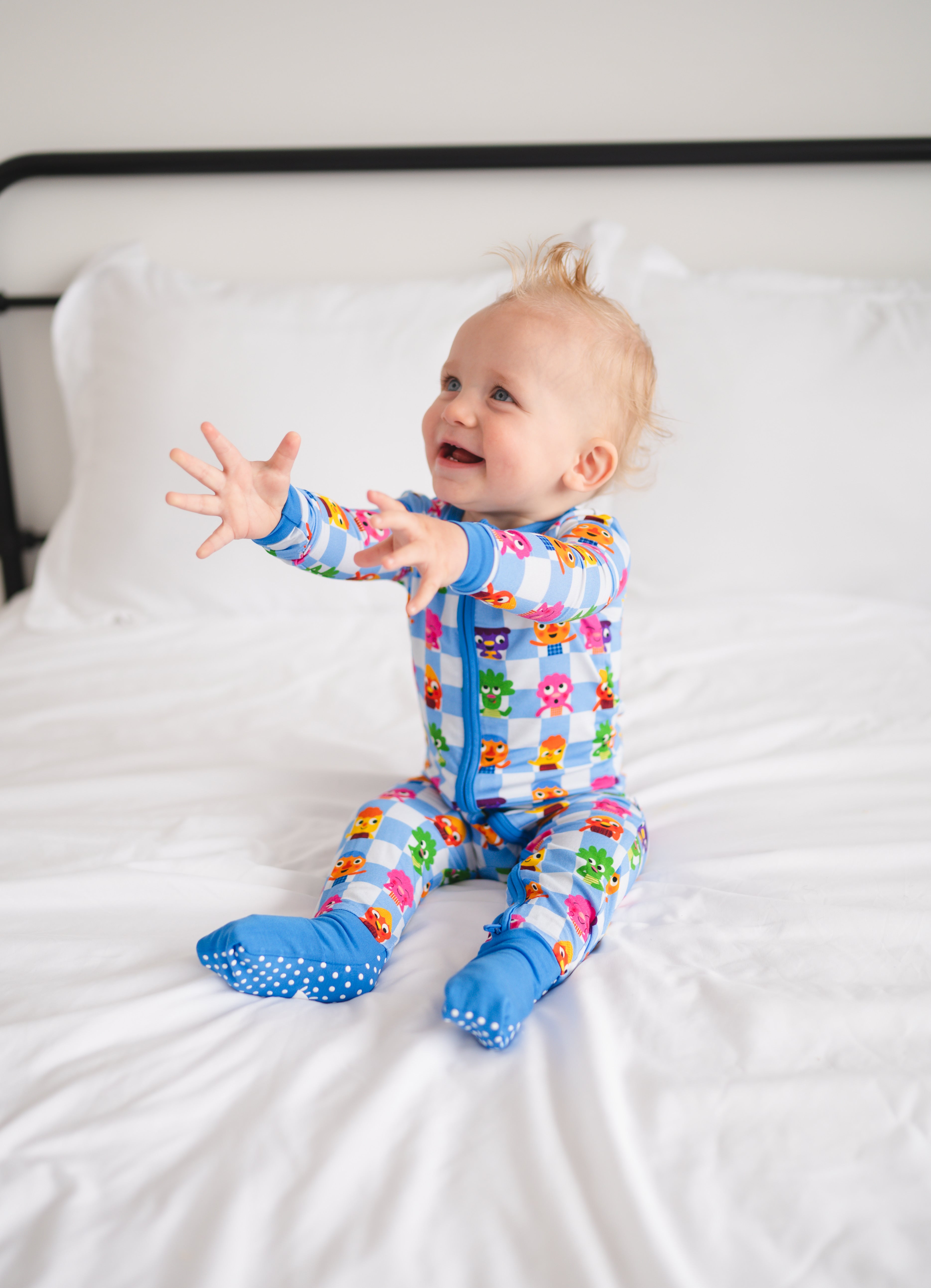 Baby in blue footie pajamas with a checkered pattern and cartoon characters.