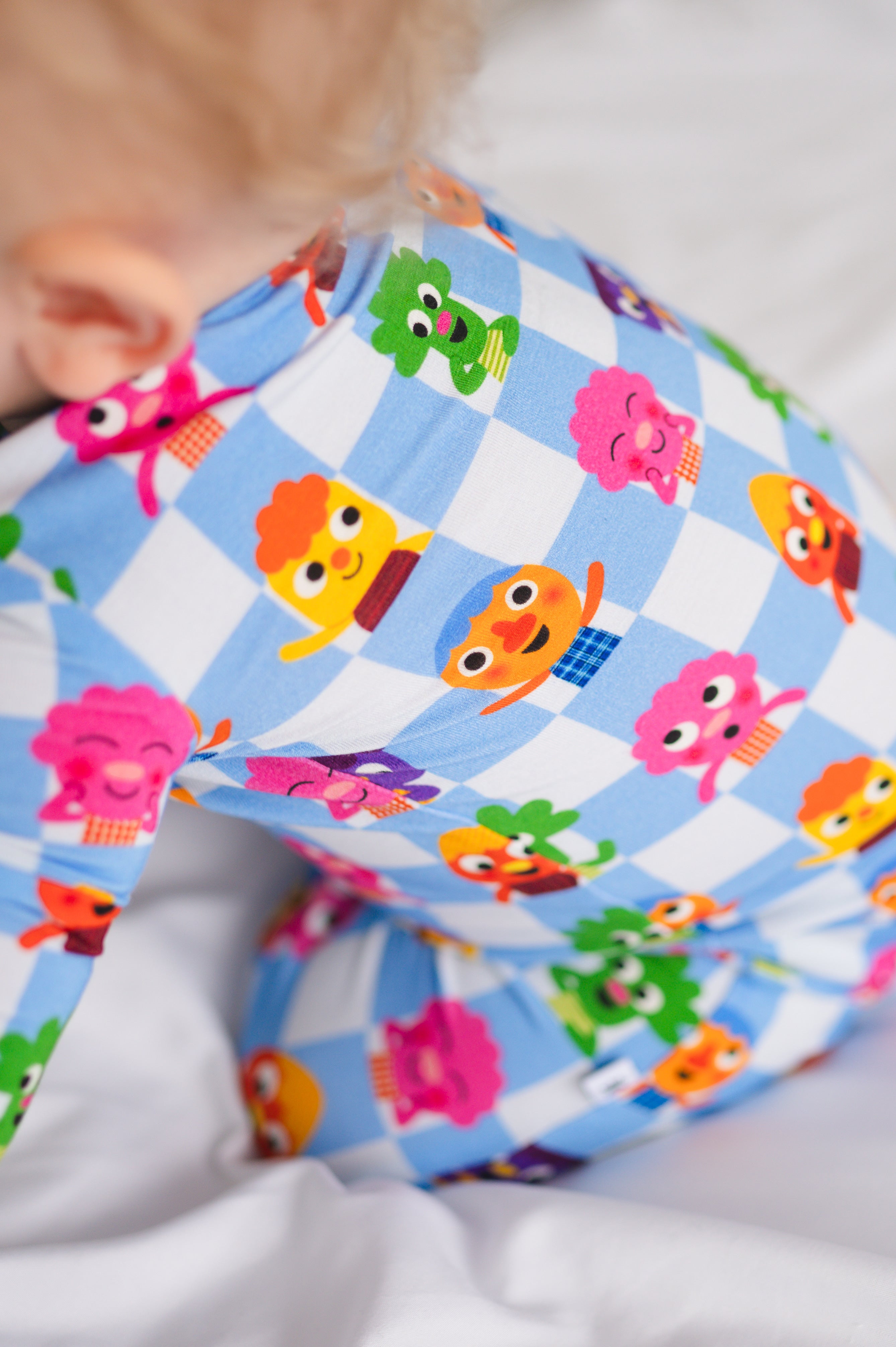 A baby wearing blue and white checkered pajamas with cartoon characters.