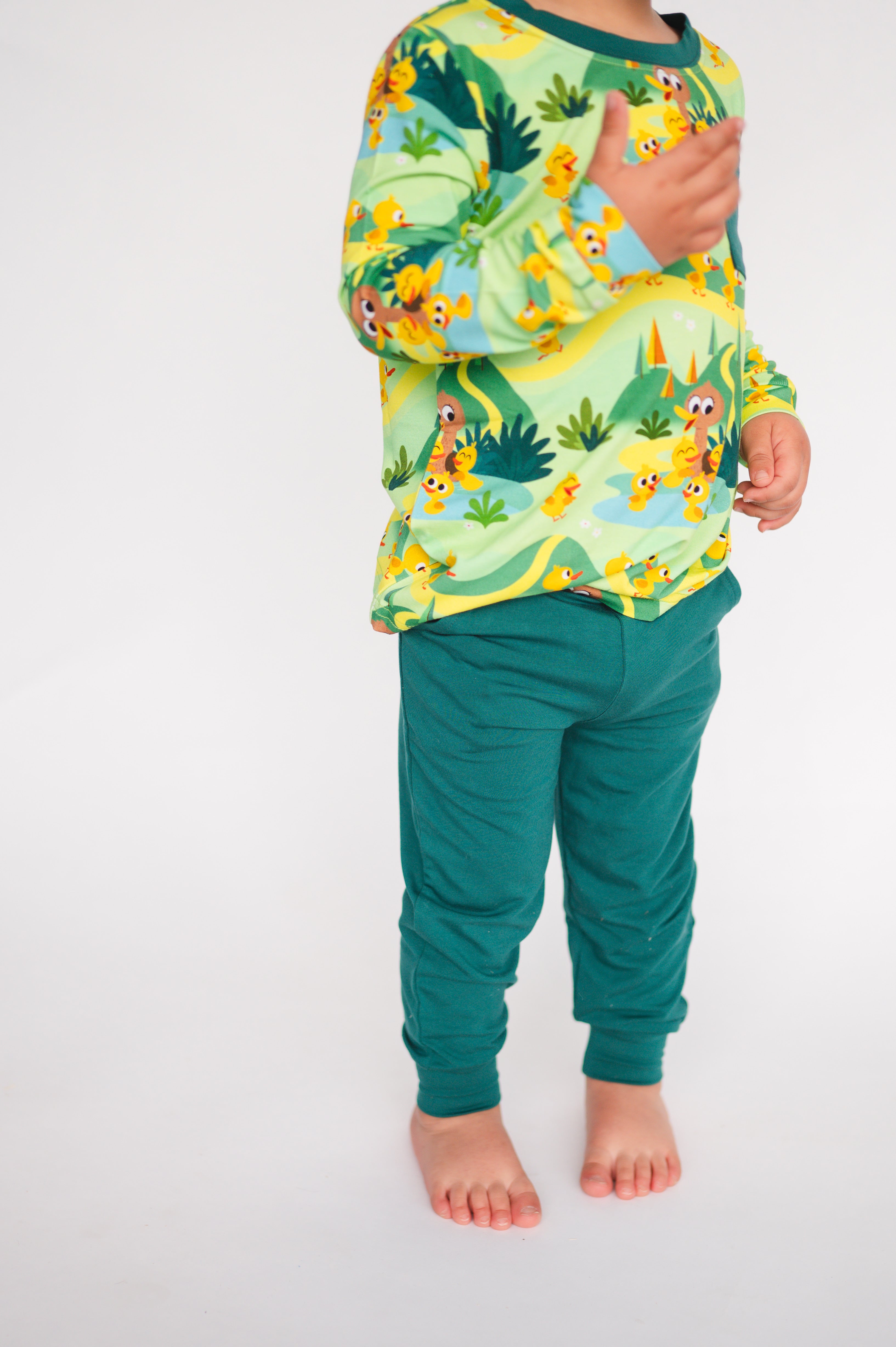 A child wears green joggers and a long-sleeved shirt with a duck pond print.