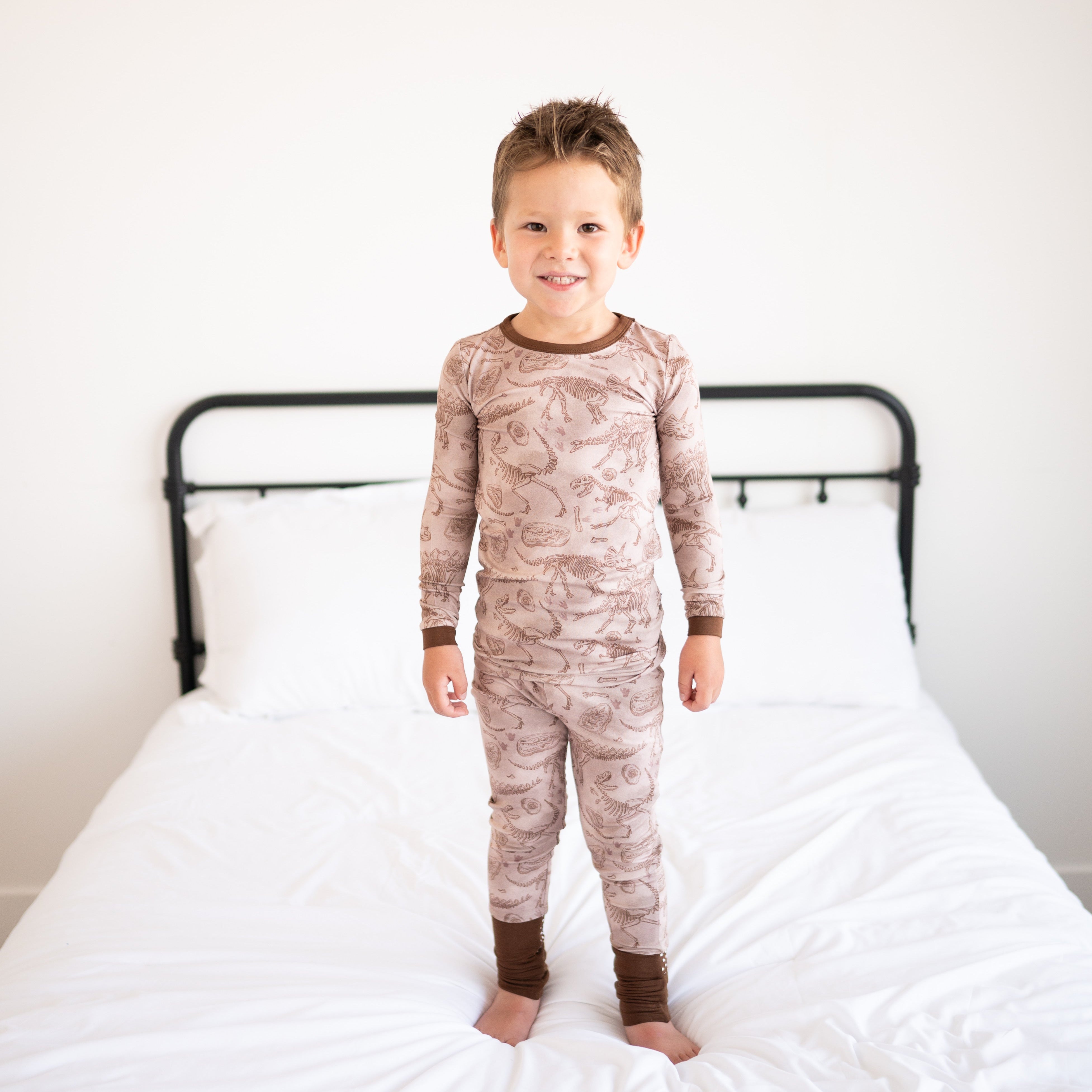 A young boy stands on a bed wearing a fossil-print pajama set.