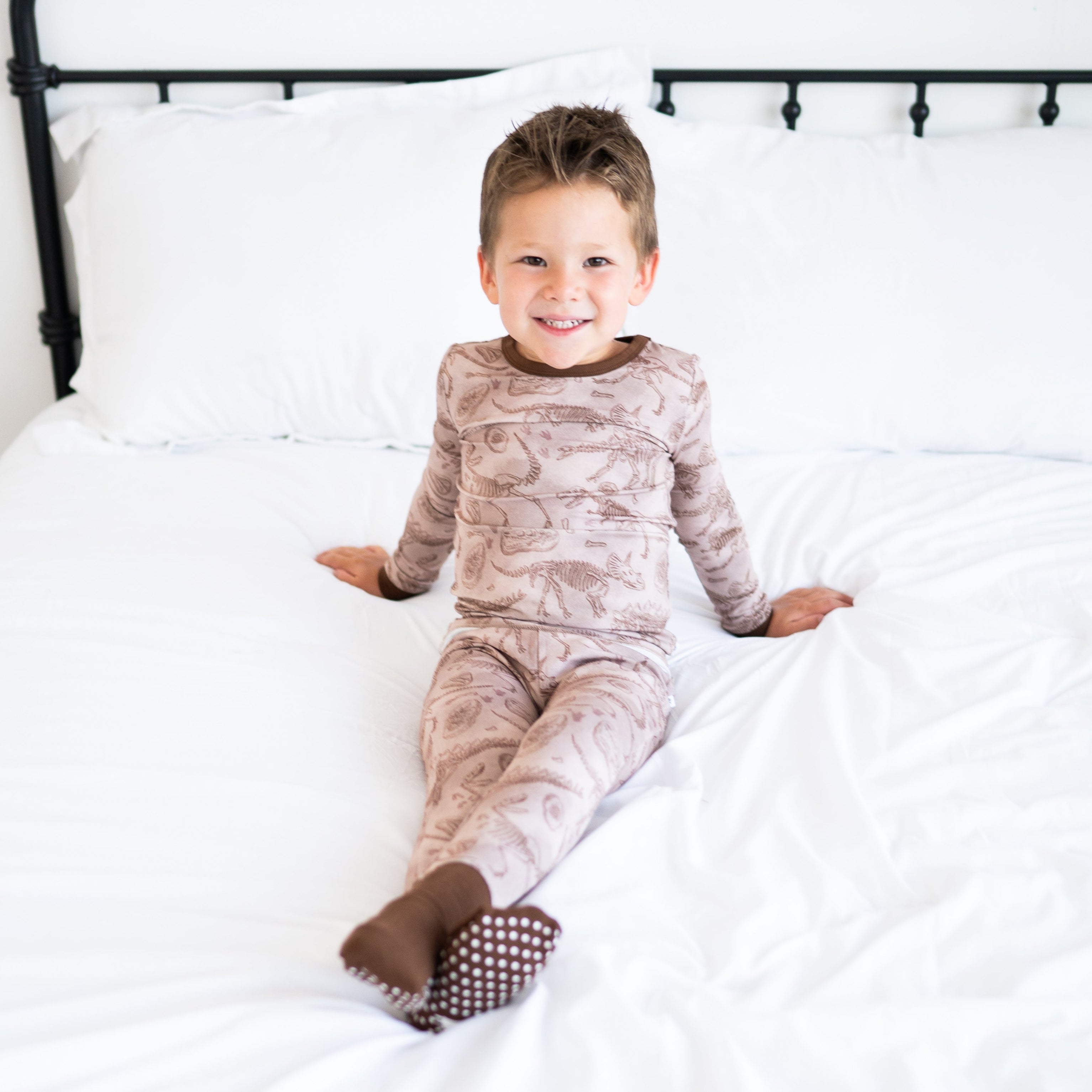 A young boy smiles while wearing a brown bamboo pajama set with a fossil print.