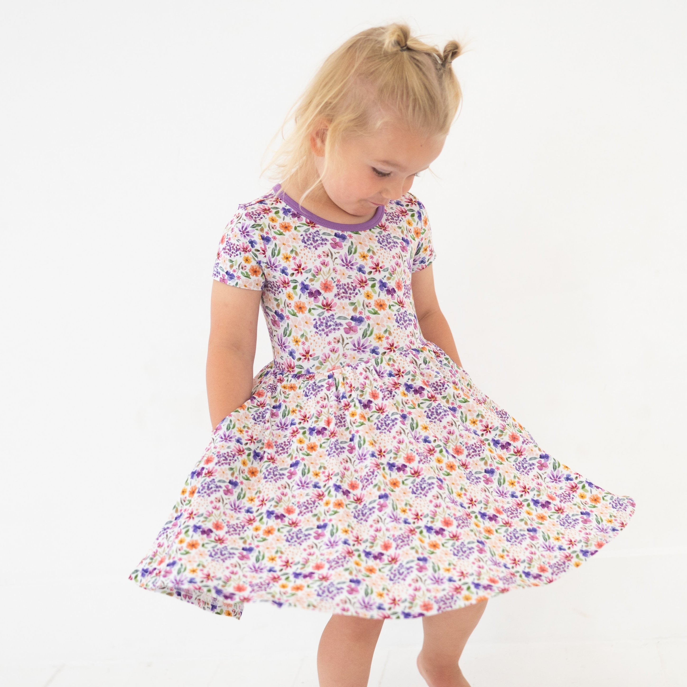 A young girl twirls in a white dress with a colorful floral print.