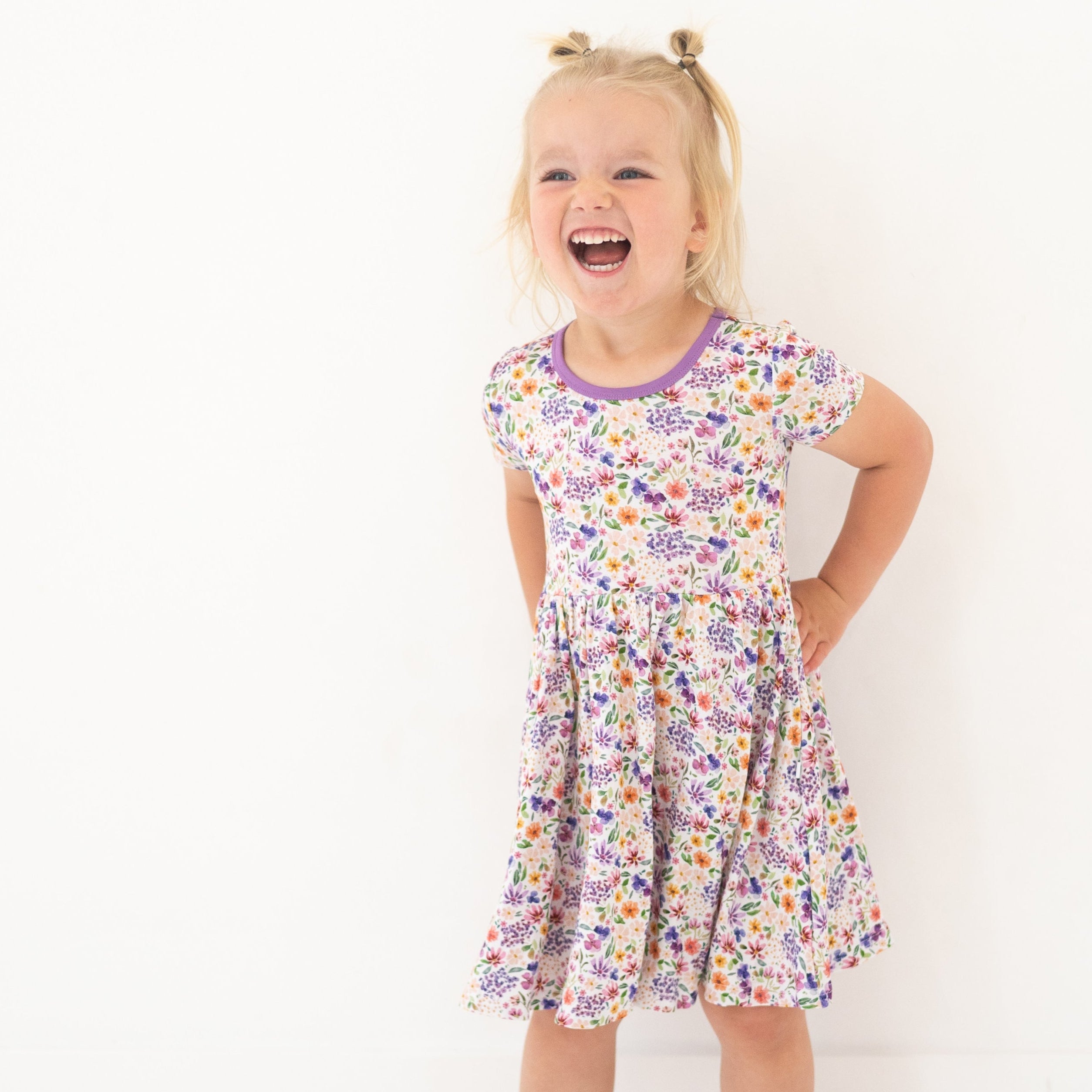A young girl laughs while wearing a floral print dress with a purple neckline.