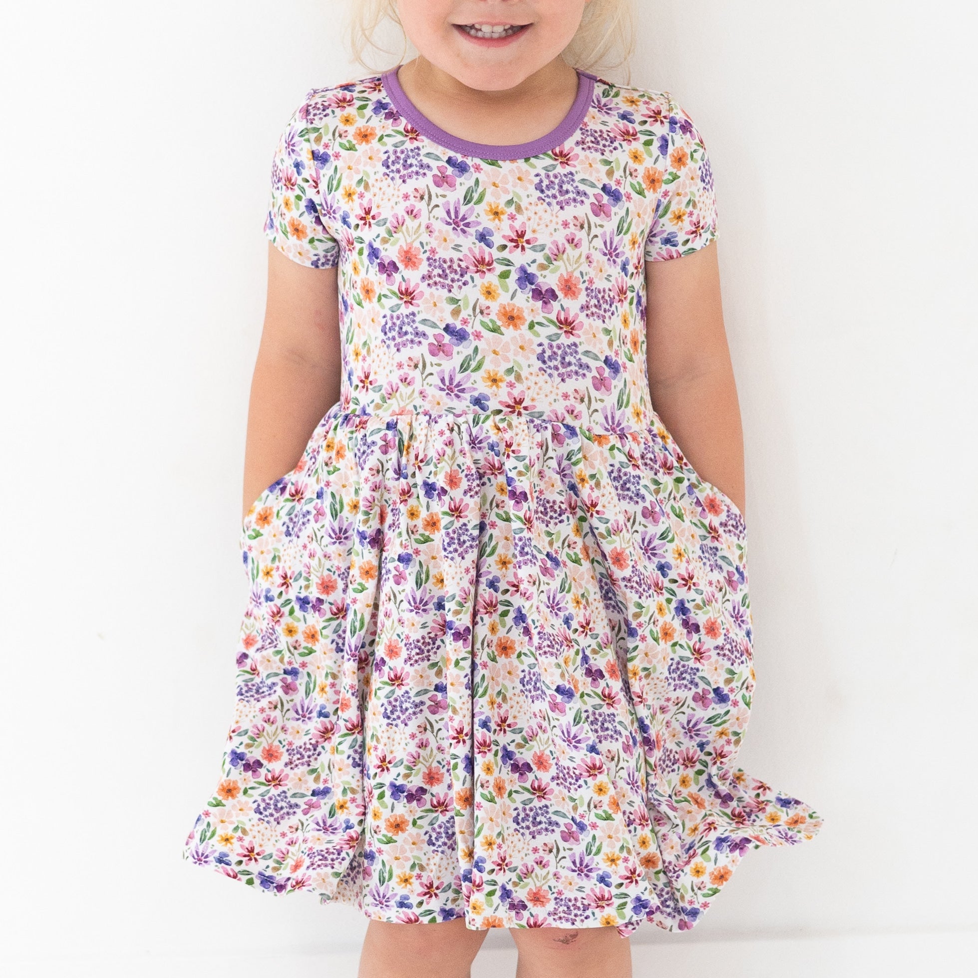 A young girl wears a white dress with a dainty floral print and purple trim.