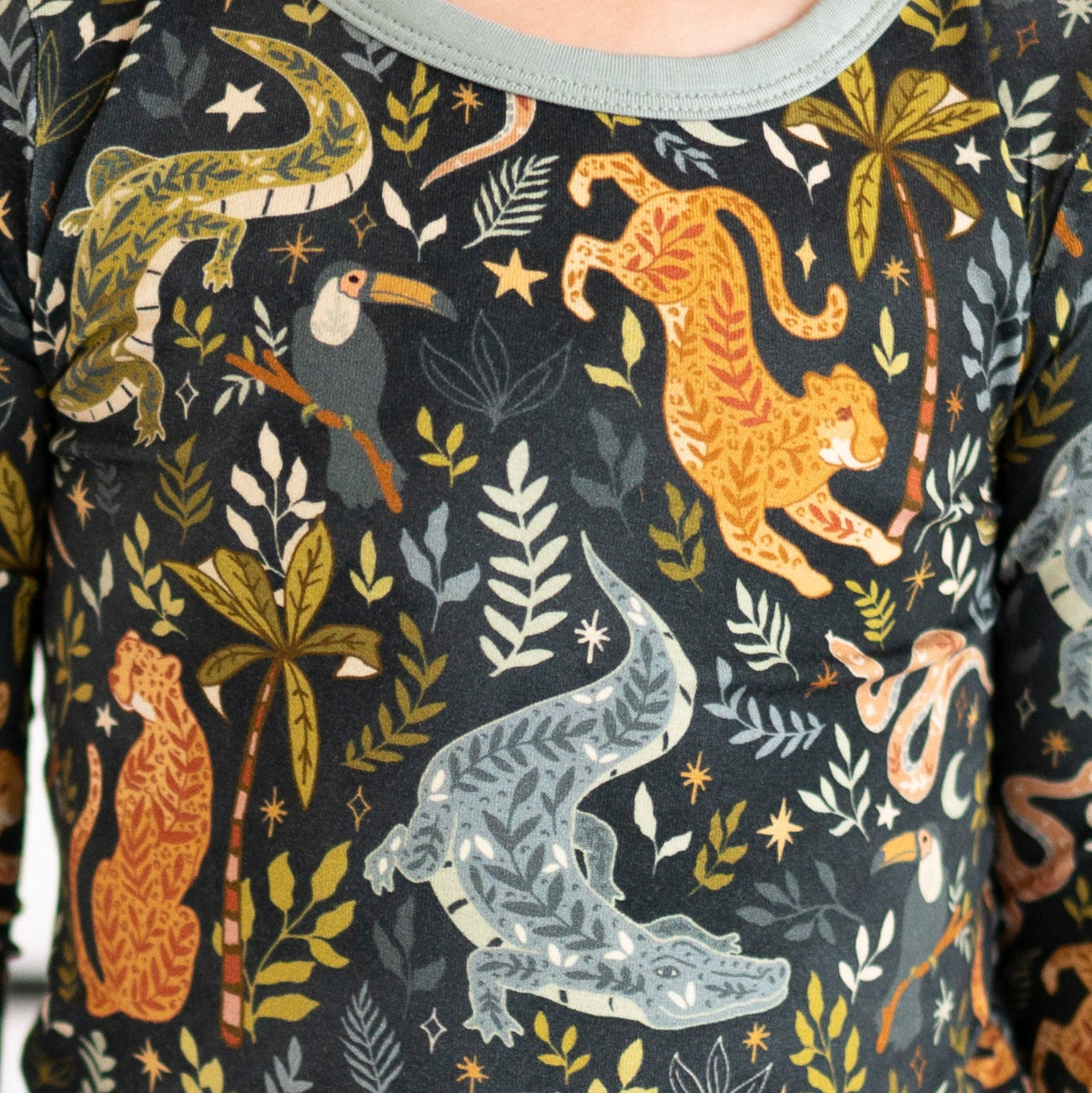 A dark grey long-sleeved pajama top with a jungle print featuring leopards, a crocodile, a lizard, a toucan, and tropical foliage.