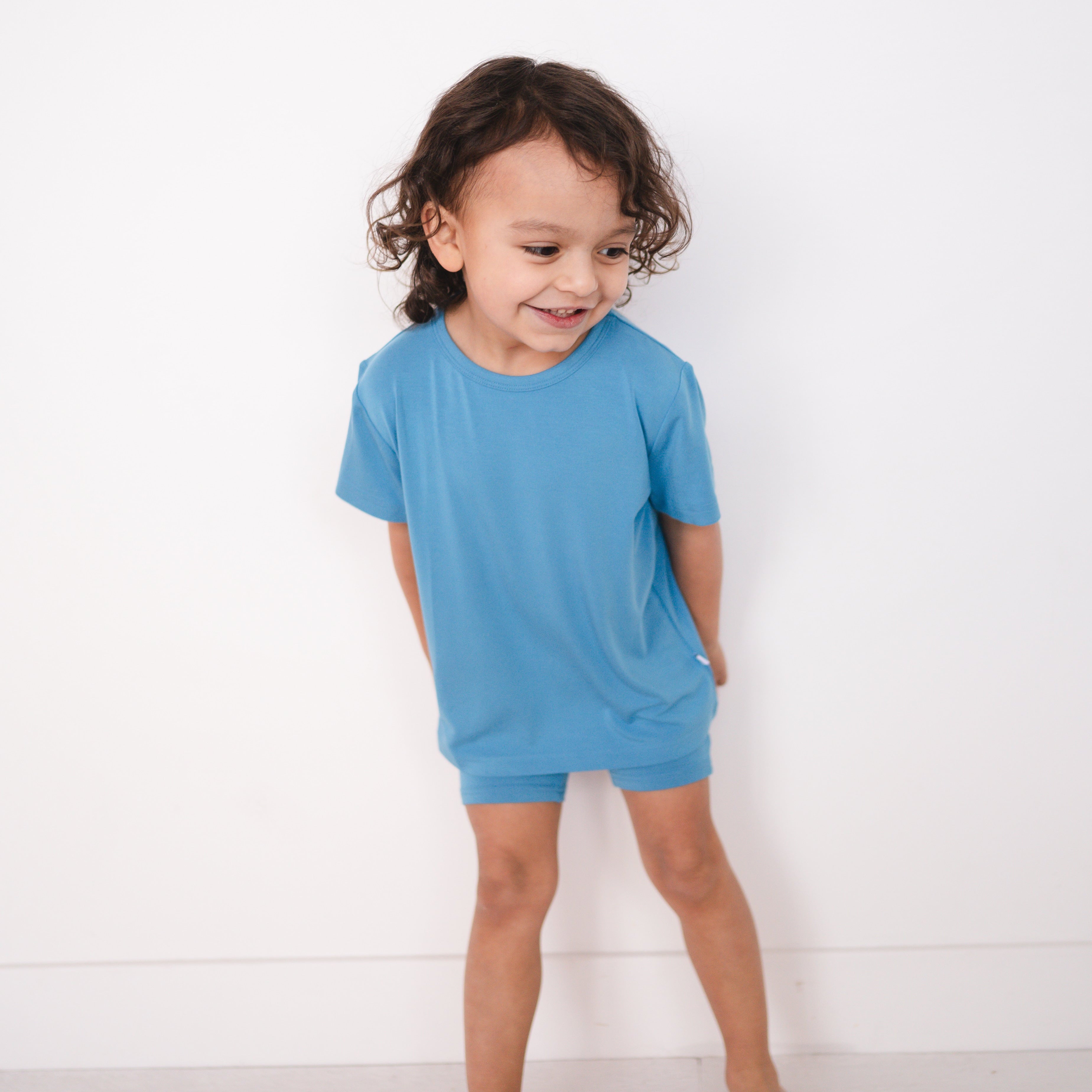 A young child wears a cornflower blue t-shirt and matching shorts.