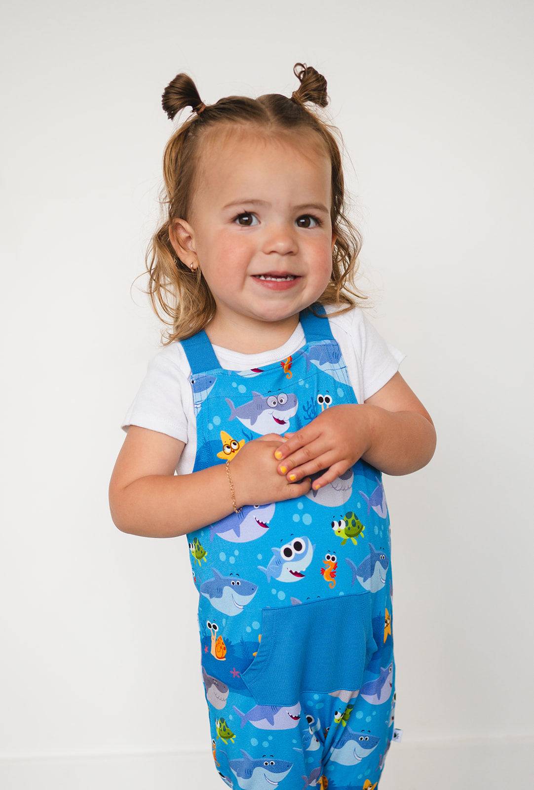A toddler girl wears blue overalls with a Baby Shark print.