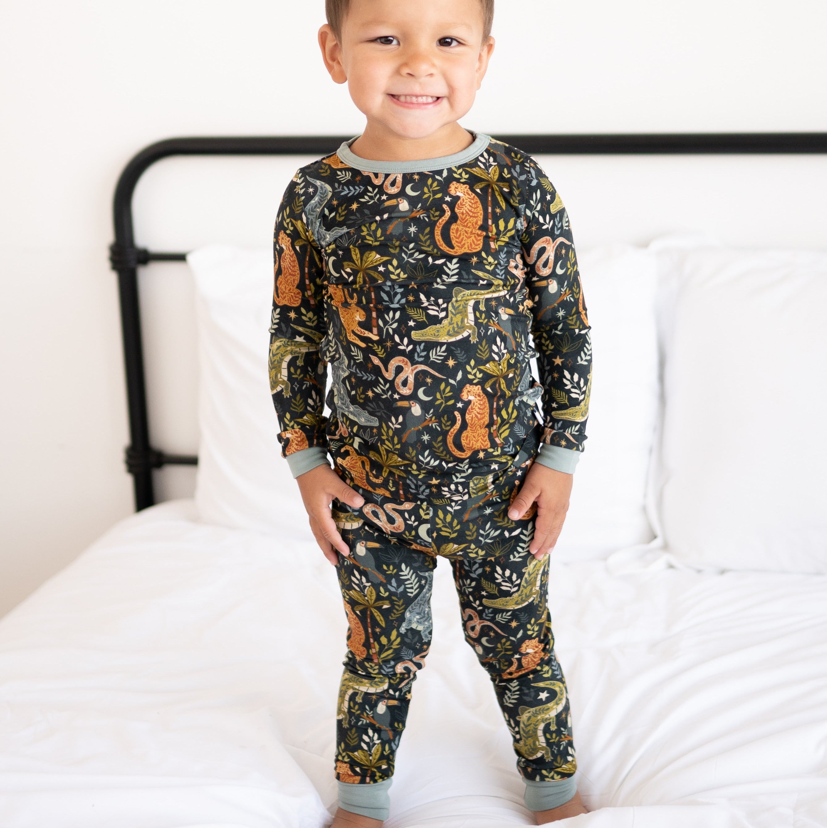 A young boy smiles wearing a long-sleeved pajama set with a night jungle print.