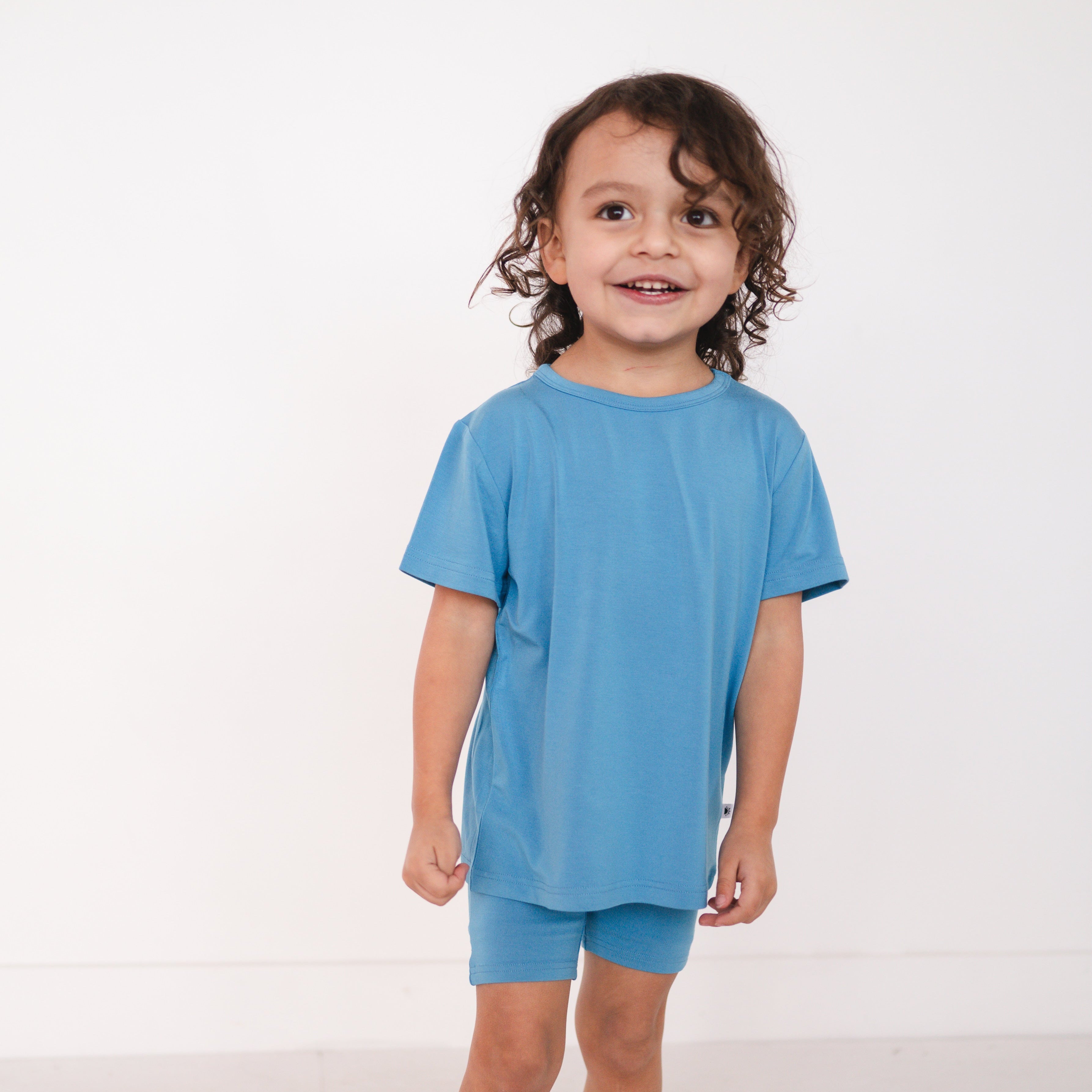 A young child wears a cornflower blue t-shirt and matching shorts.
