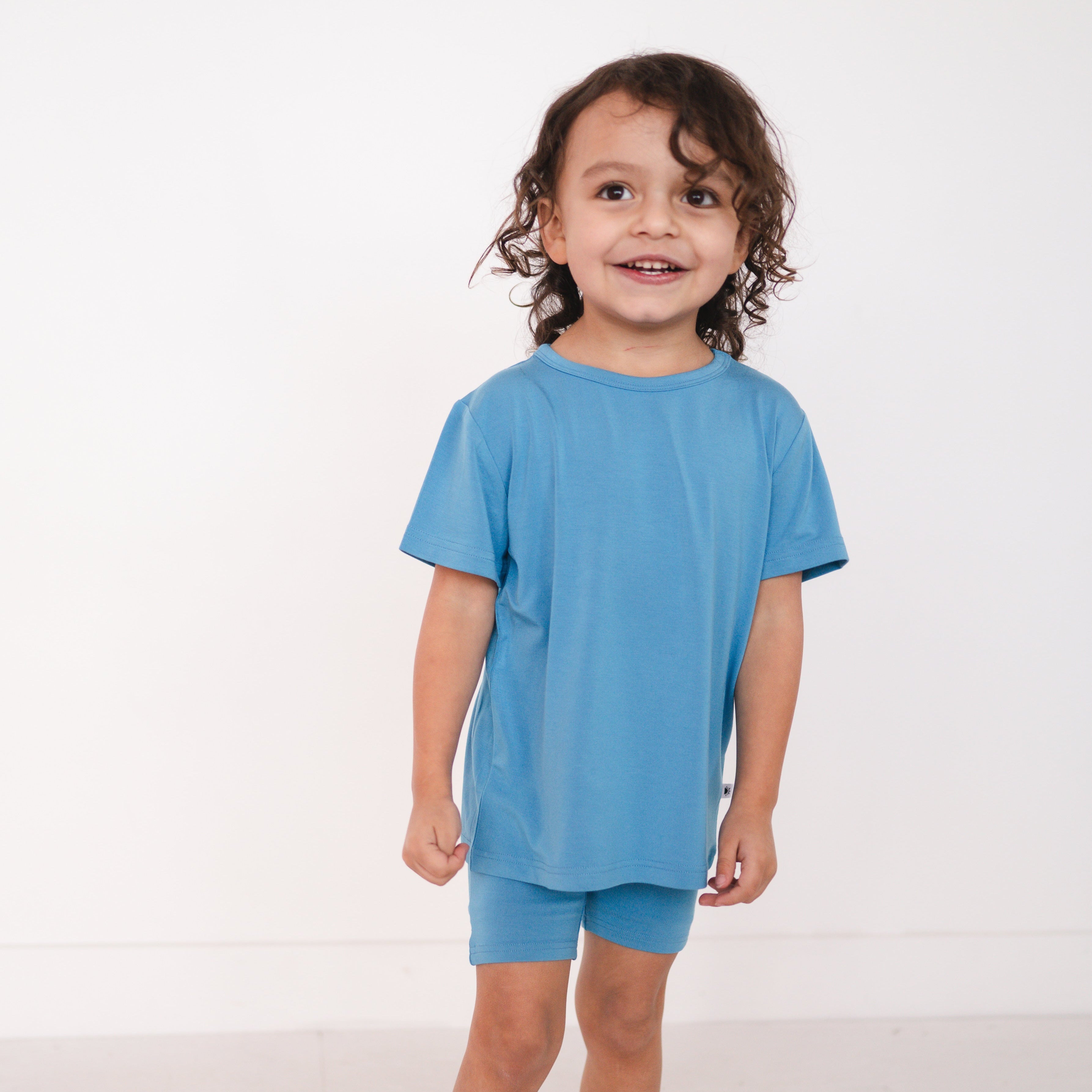 A young child wears a cornflower blue t-shirt and matching biker shorts.