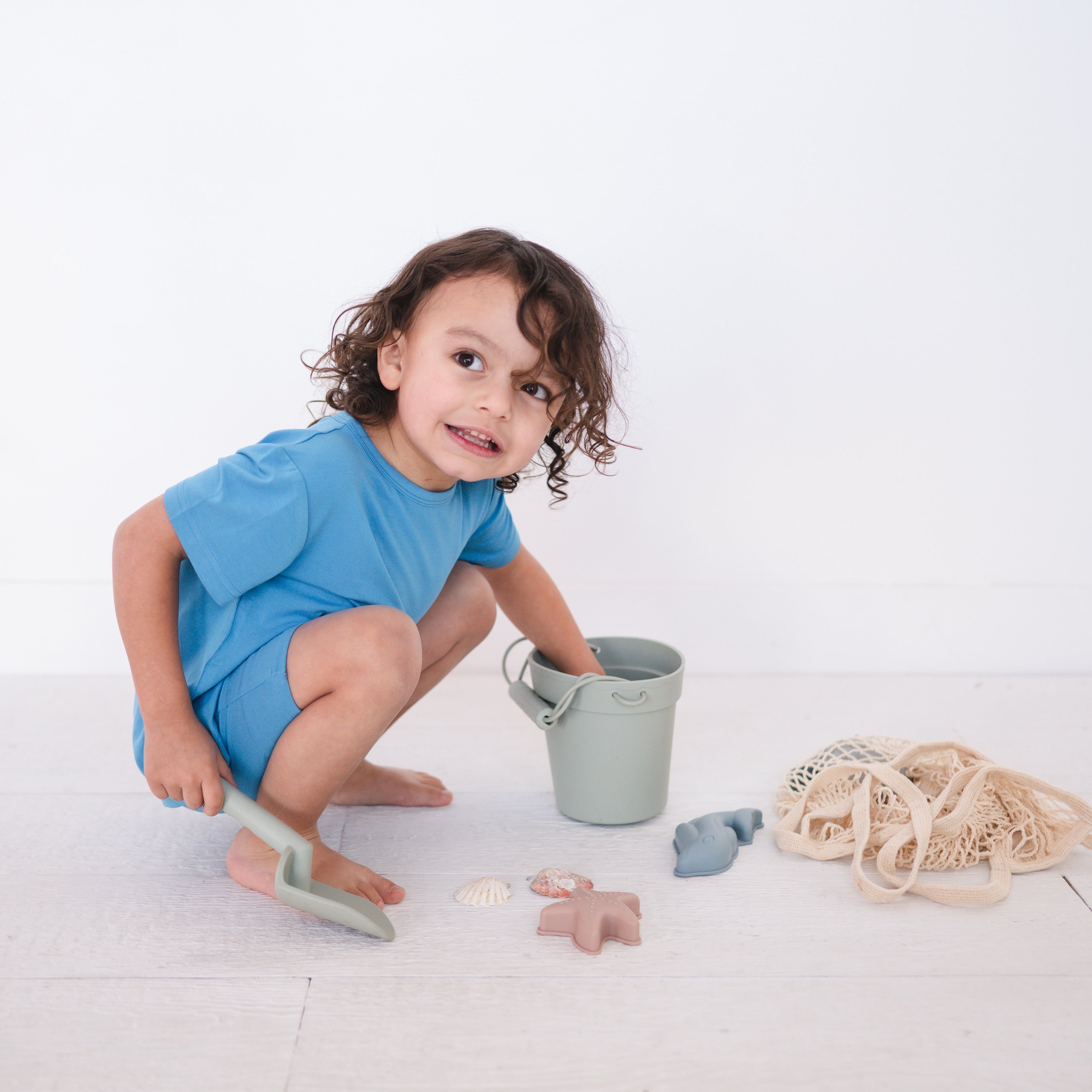 A young child in a cornflower blue t-shirt plays with beach toys.