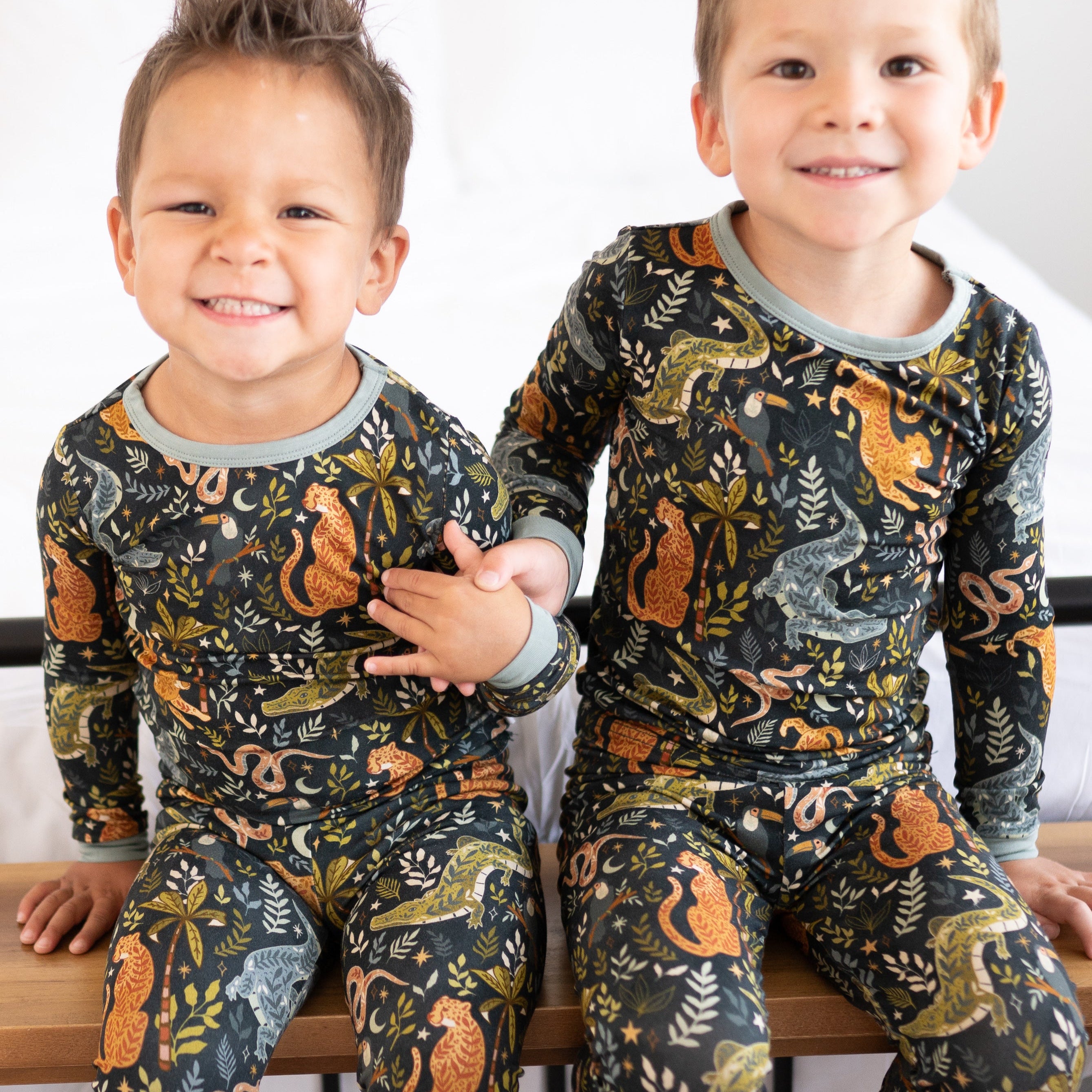 Two young boys in matching long-sleeved pajamas with a dark jungle print.