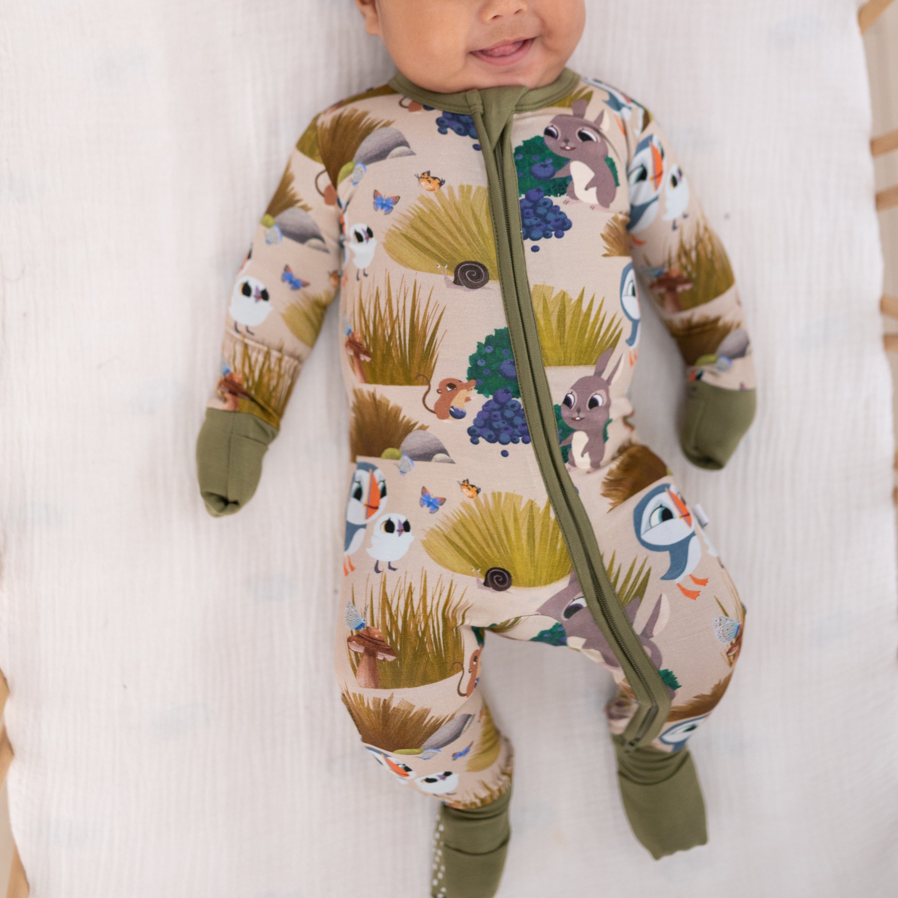A baby wearing a tan footed pajama set with a Puffin Rock print.