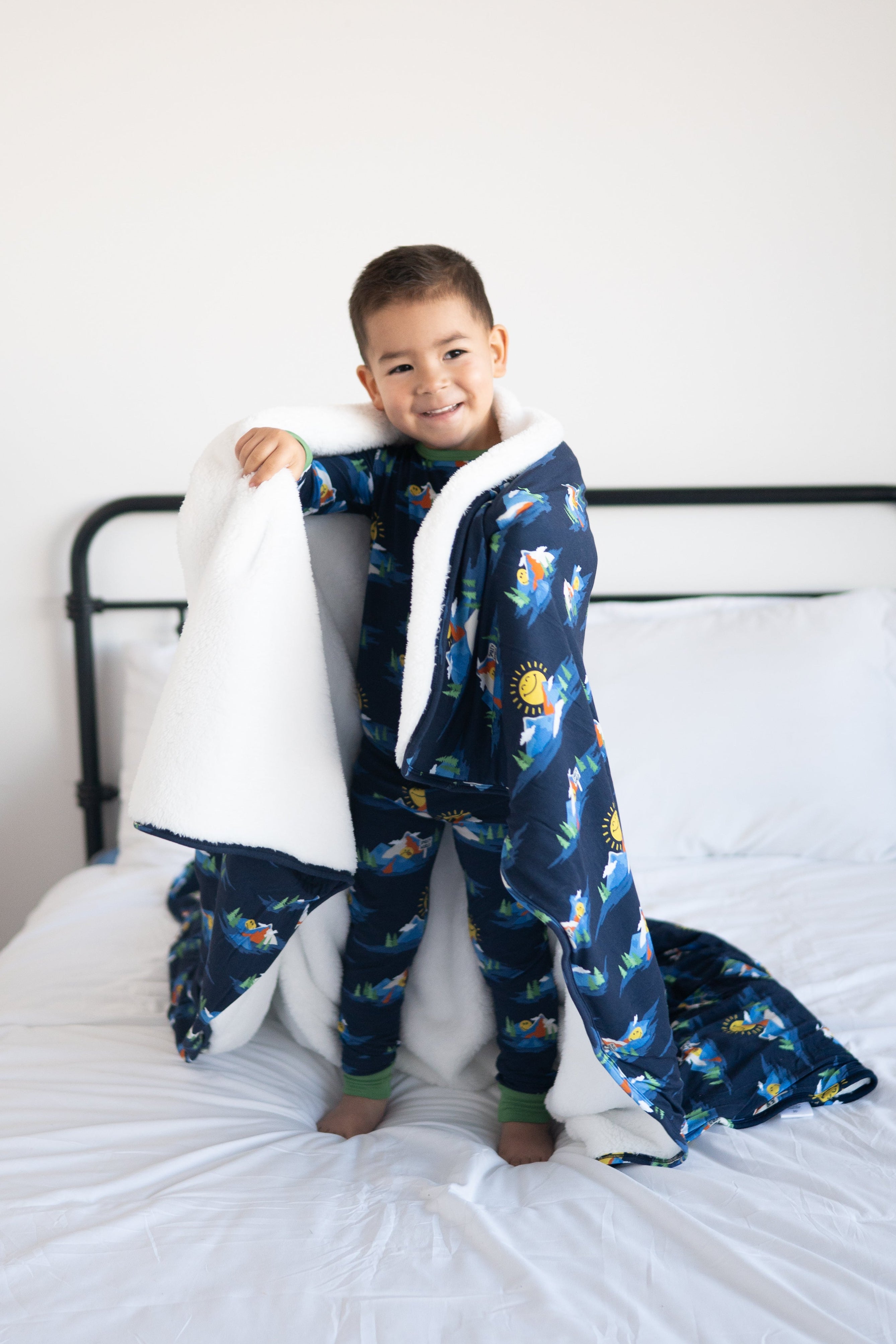 A young boy smiles while wrapped in a navy blue blanket with a SmileyWorld print and white plush trim.