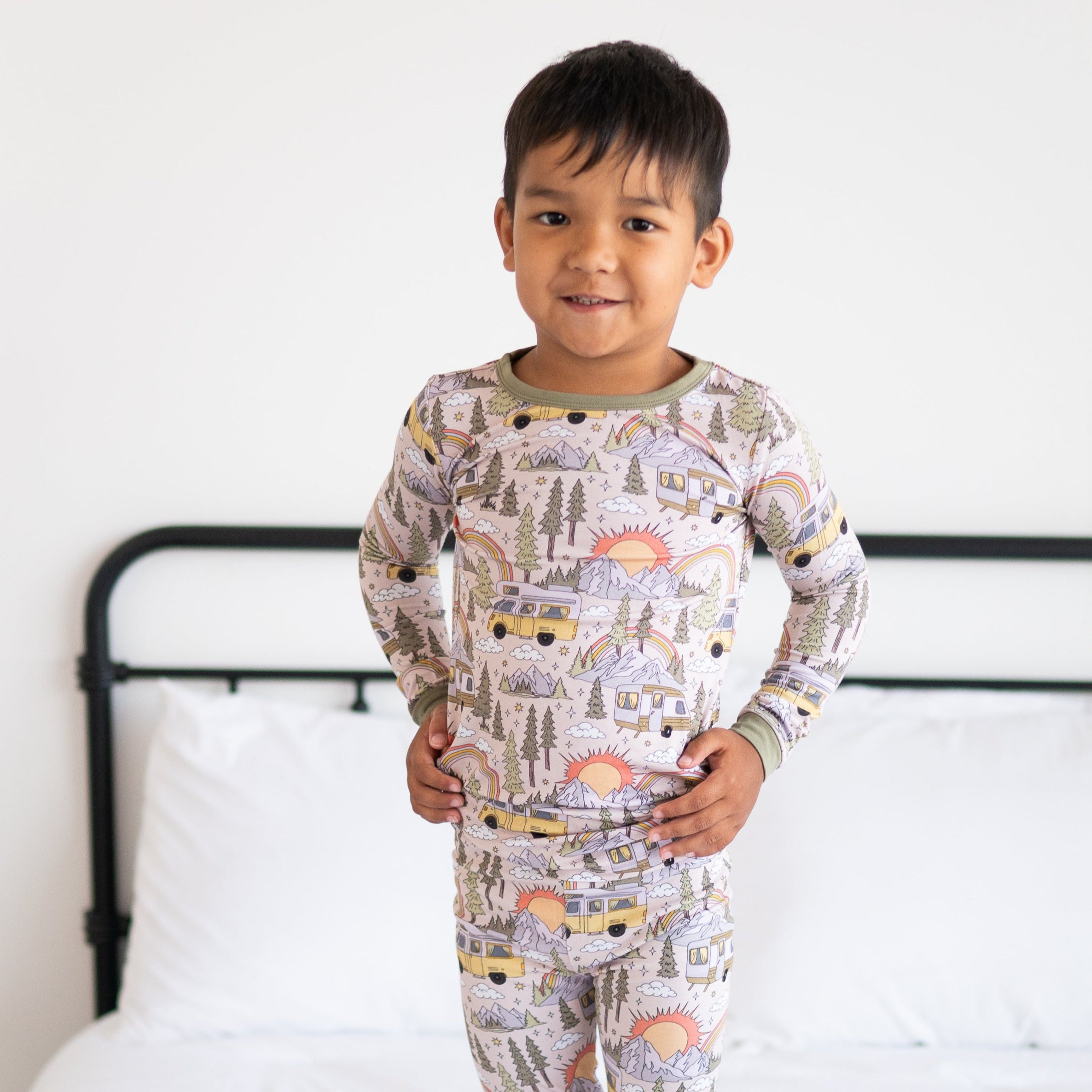 A young boy stands in a beige pajama set with a vintage camper and nature print.