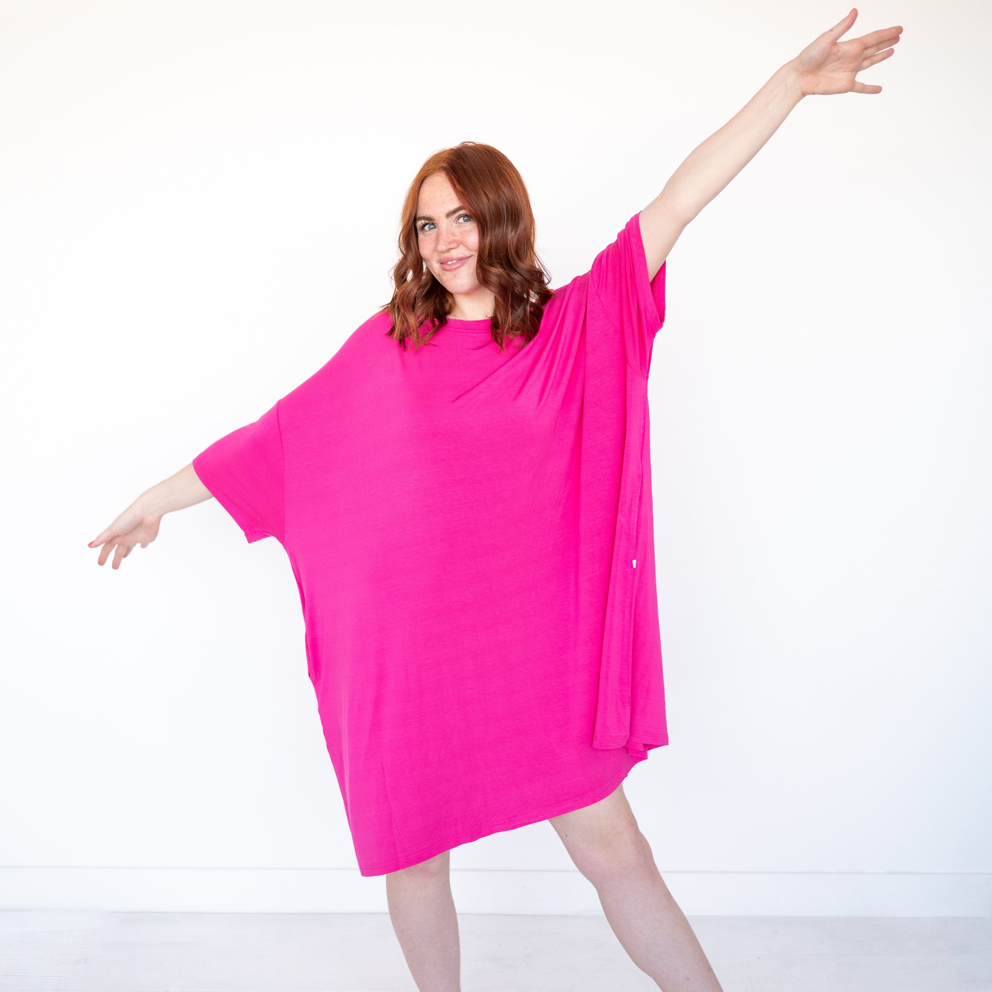 A woman in a bright pink oversized sleep tee with her arms outstretched.