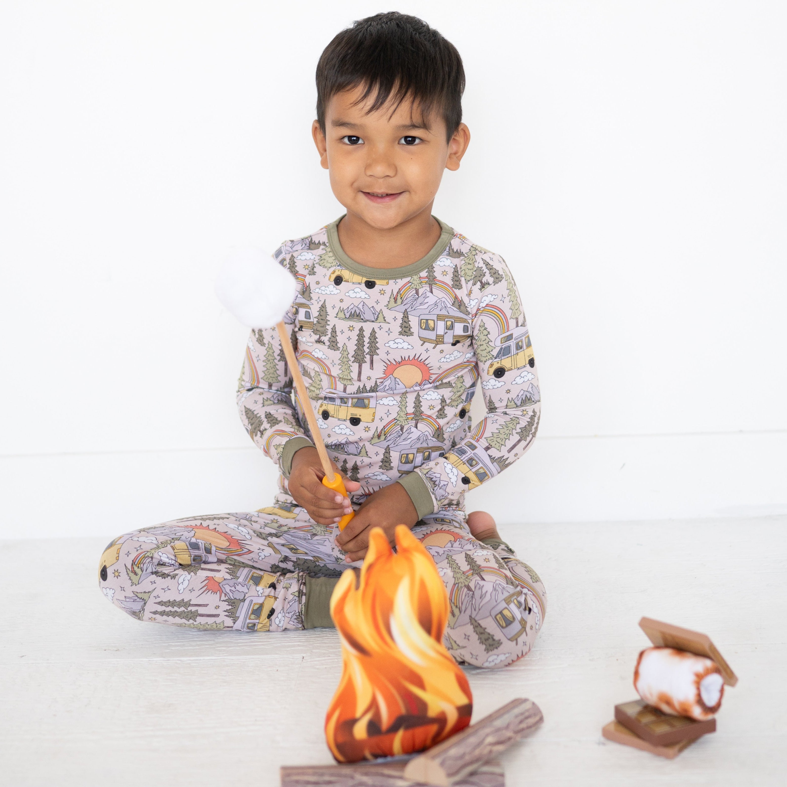 A young boy in vintage camper pajamas holds a marshmallow over a toy campfire.