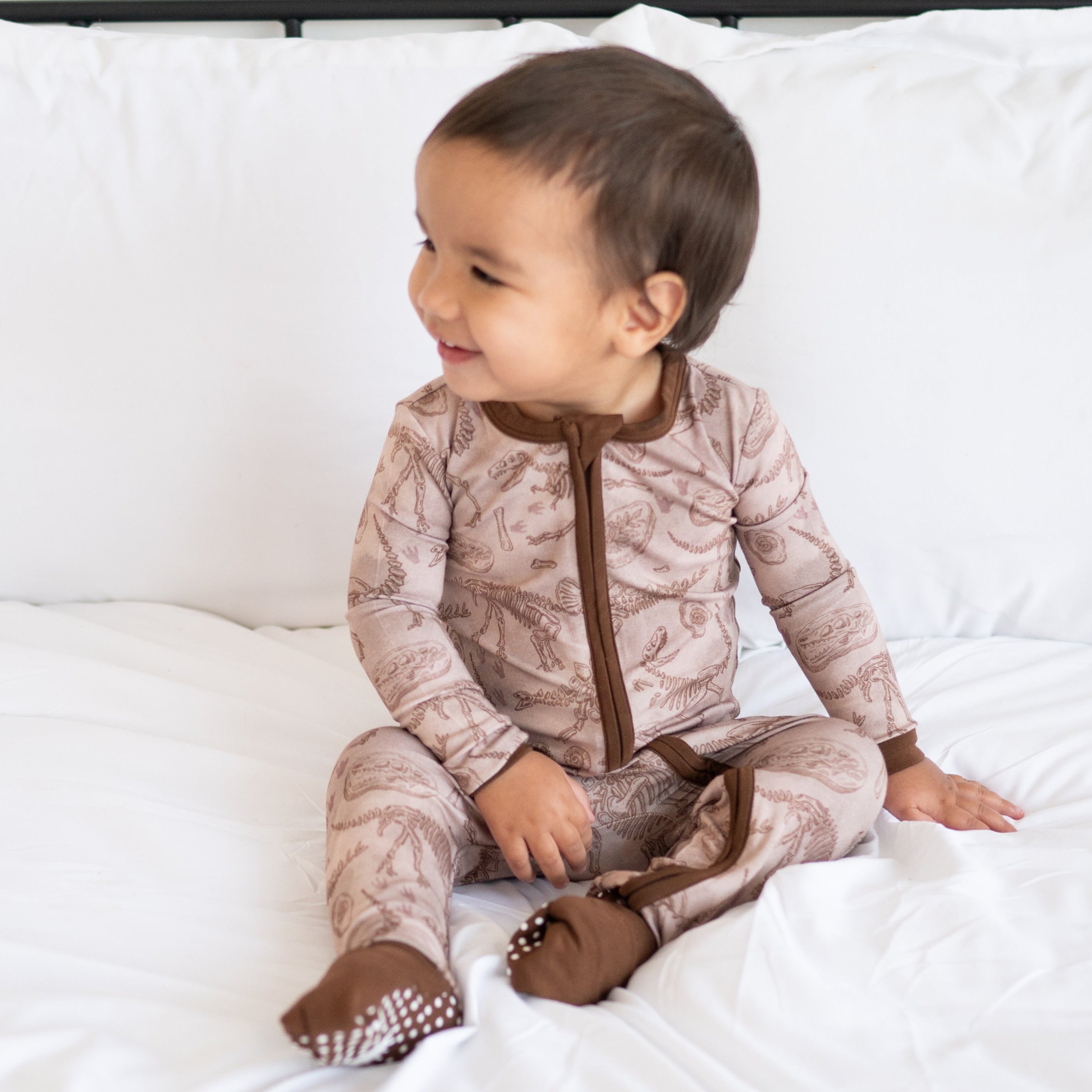 A baby wearing a brown bamboo pajama set with a fossil print.