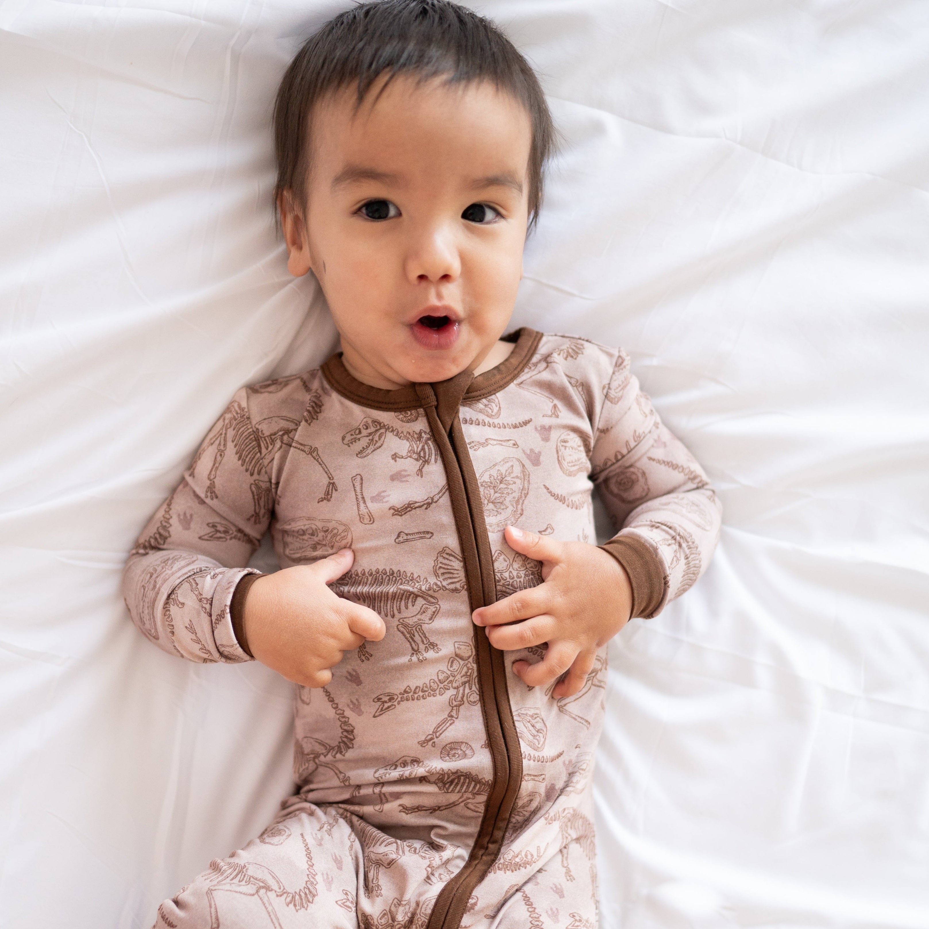A baby wearing a tan bamboo pajama set with a fossil print.