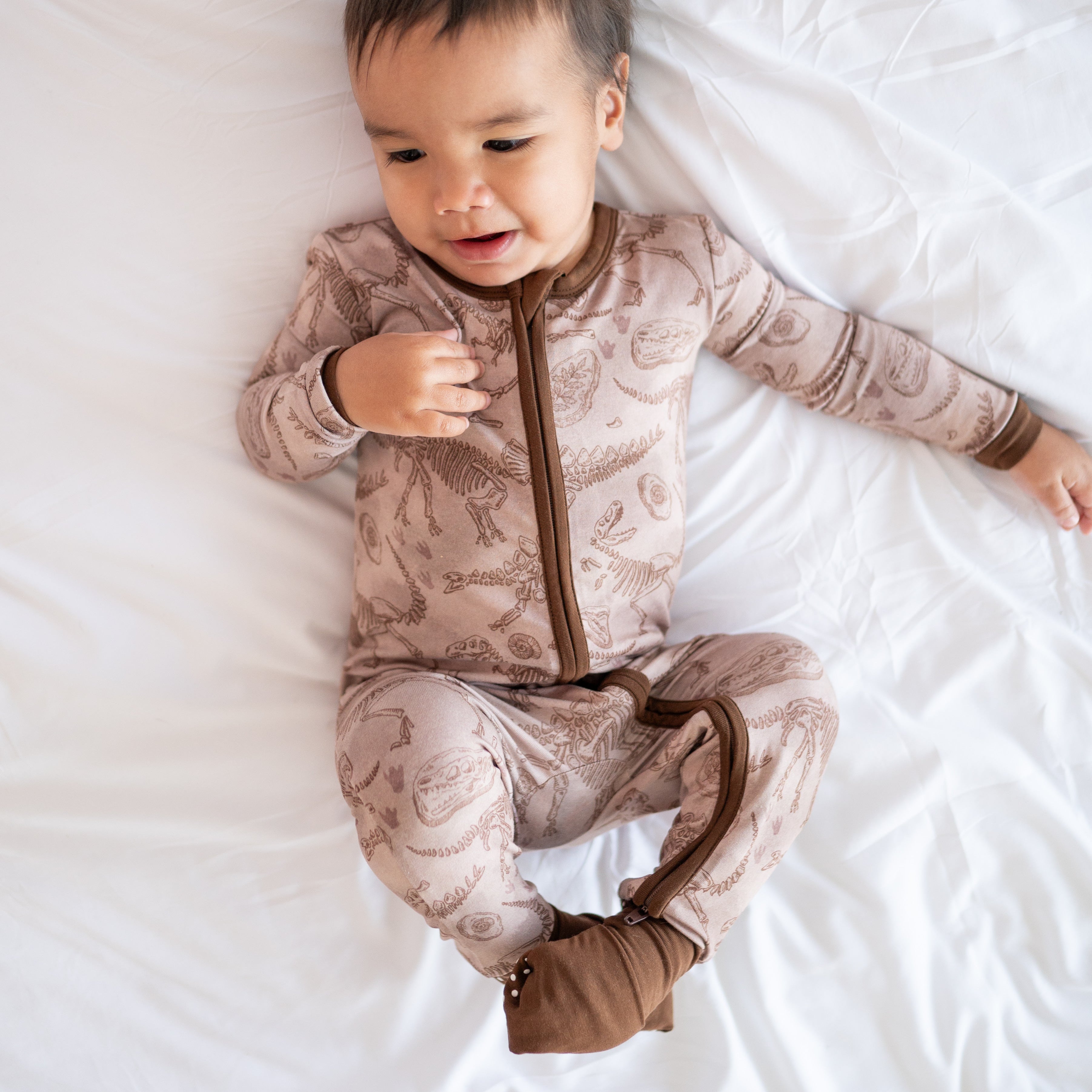 A baby wearing a tan bamboo pajama set with a fossil print.