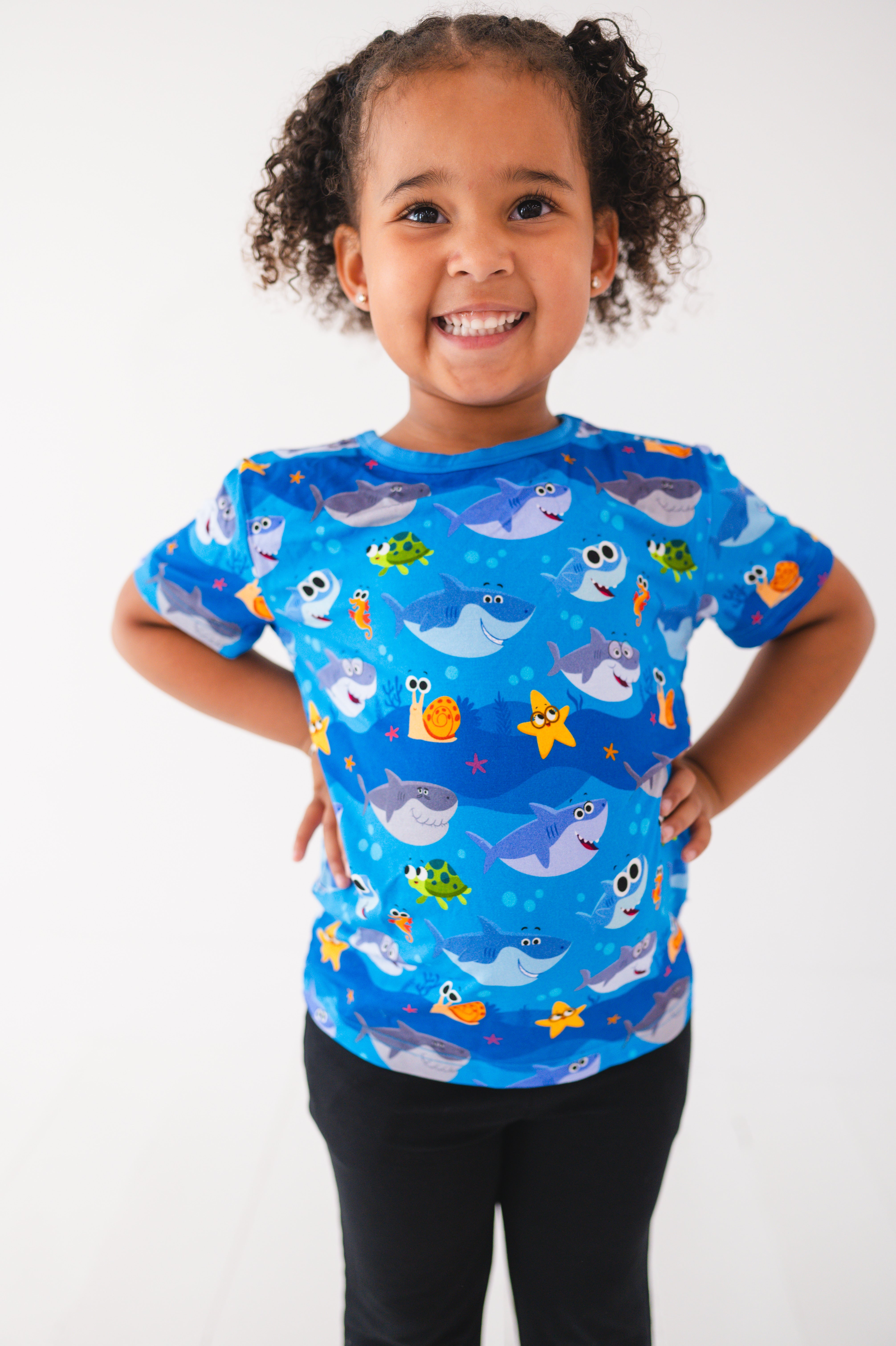 A young girl smiles wearing a blue t-shirt with a baby shark print.