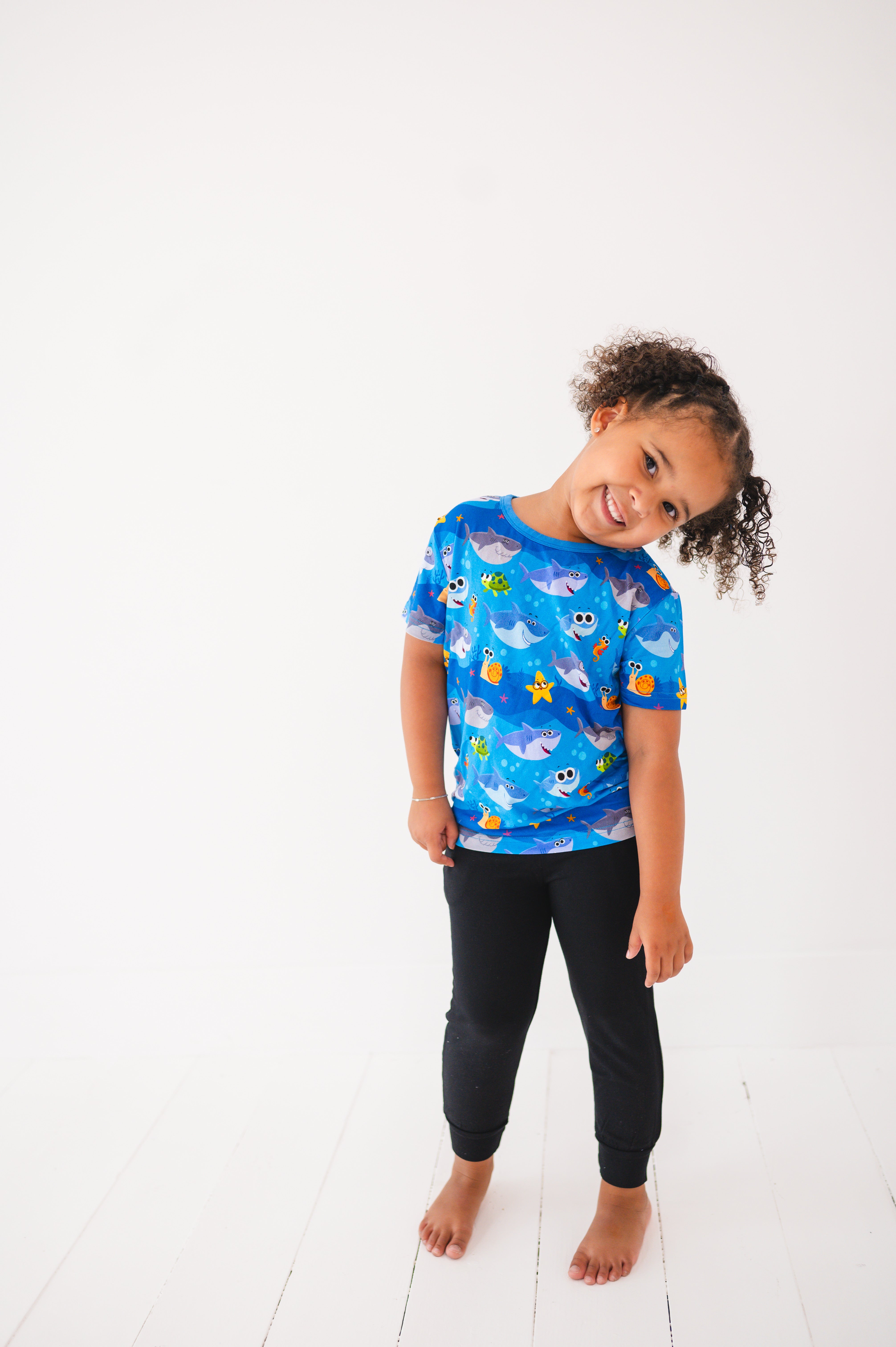 A young girl wears a blue t-shirt with a Baby Shark print and black pants.