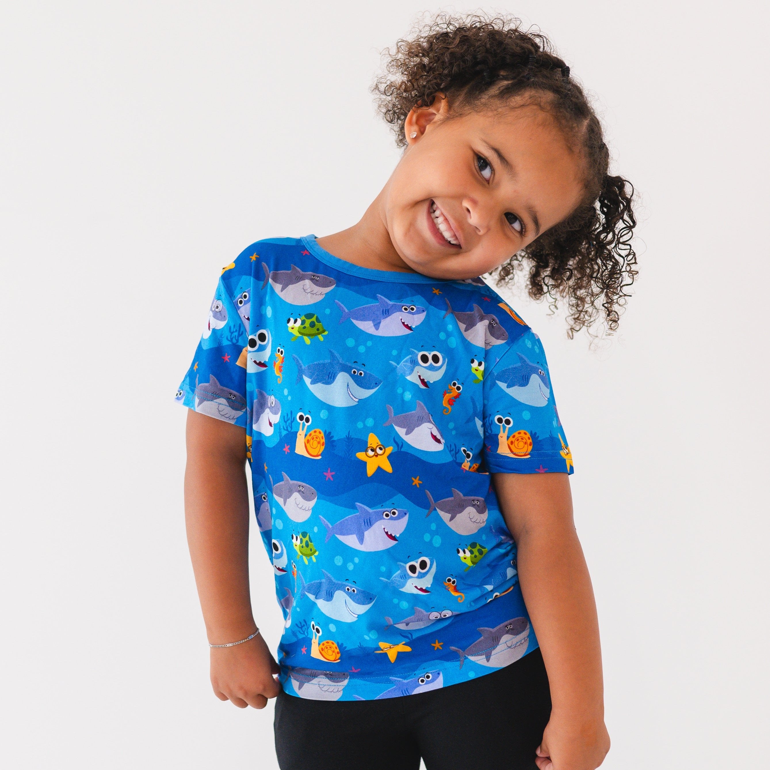 A young girl smiles wearing a blue t-shirt with a Baby Shark print.