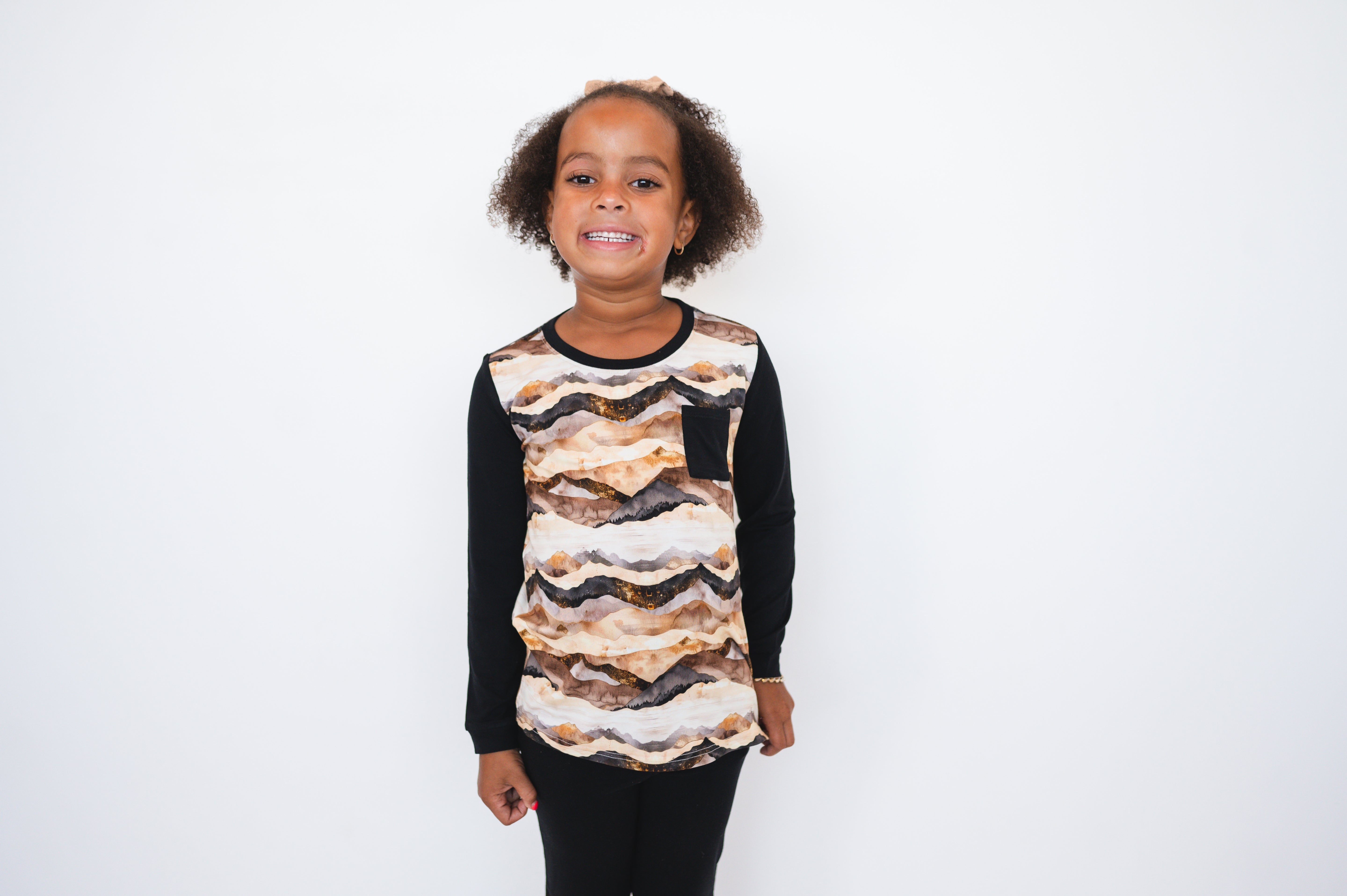 A young girl wears a long-sleeved shirt with a mountain range print and black sleeves.