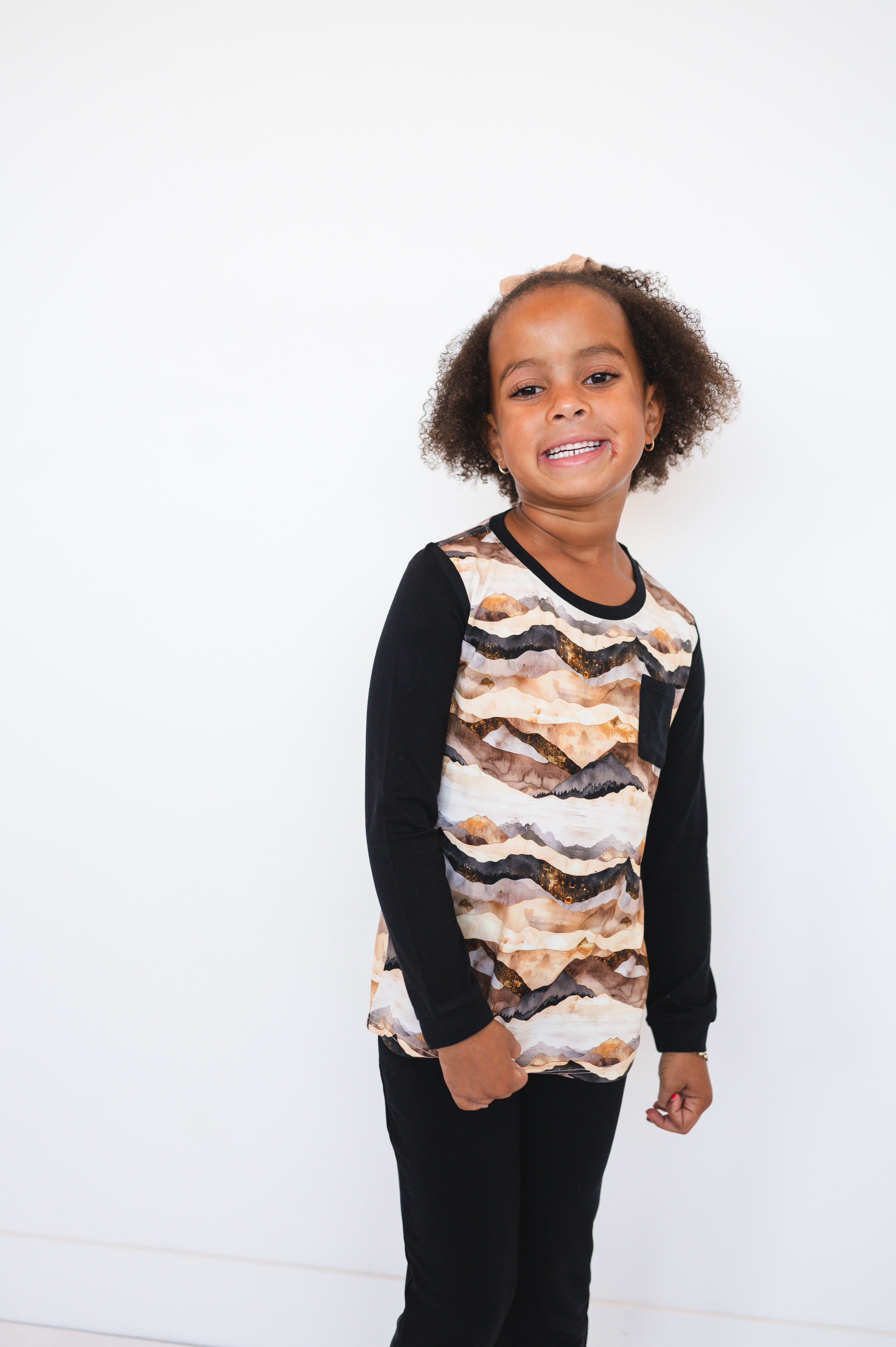 A young girl wears a long-sleeved shirt with a mountain range print and black sleeves.