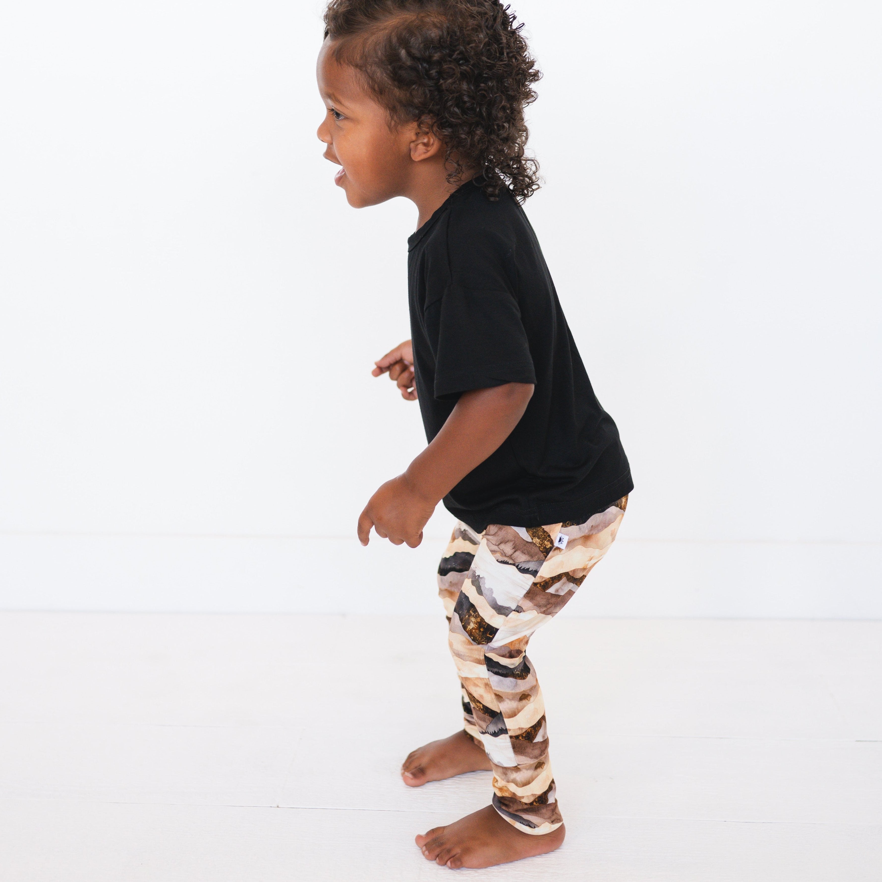 A young child wears black t-shirt and mountain range print bamboo pants.