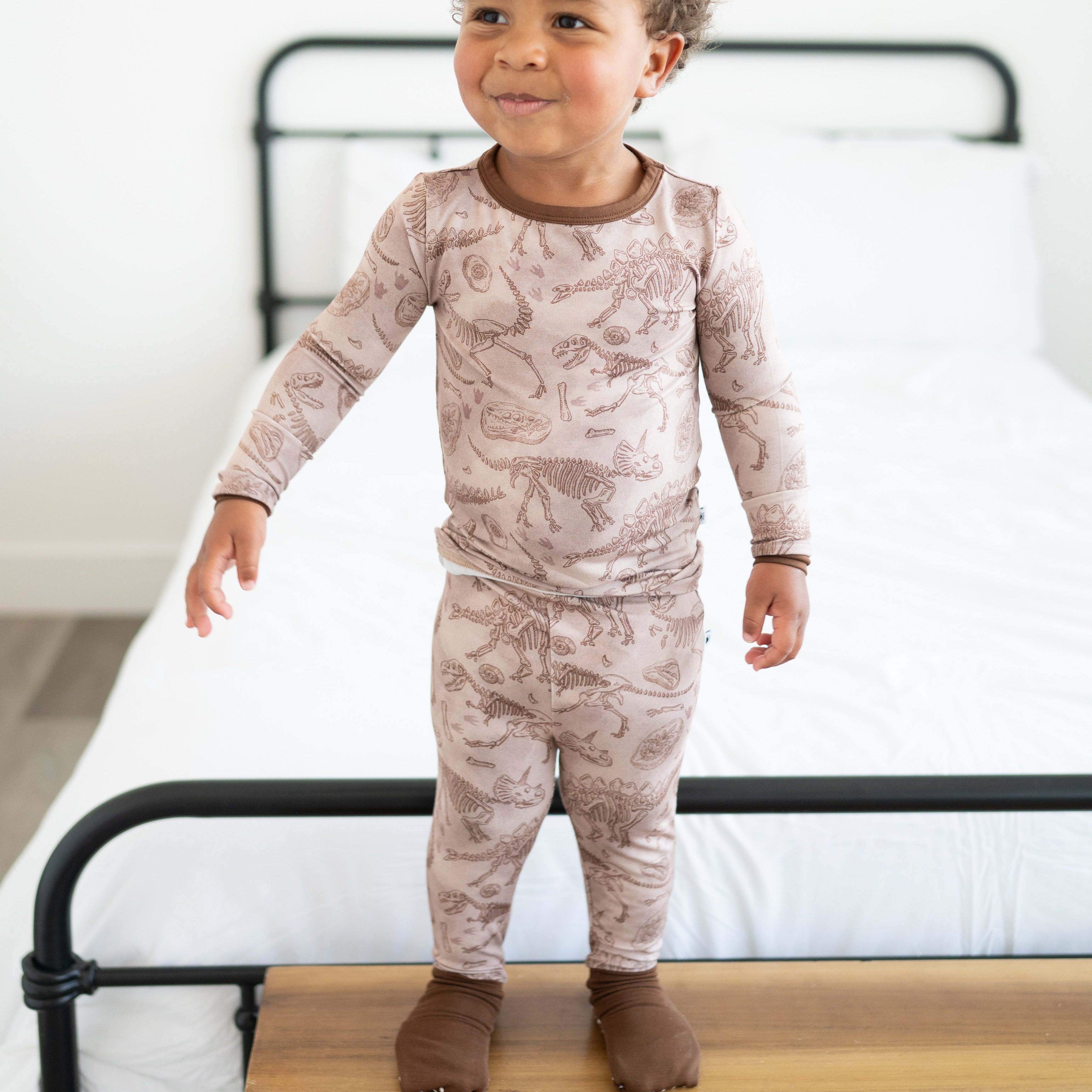 A young child wears a long-sleeved pajama set with a fossil print.