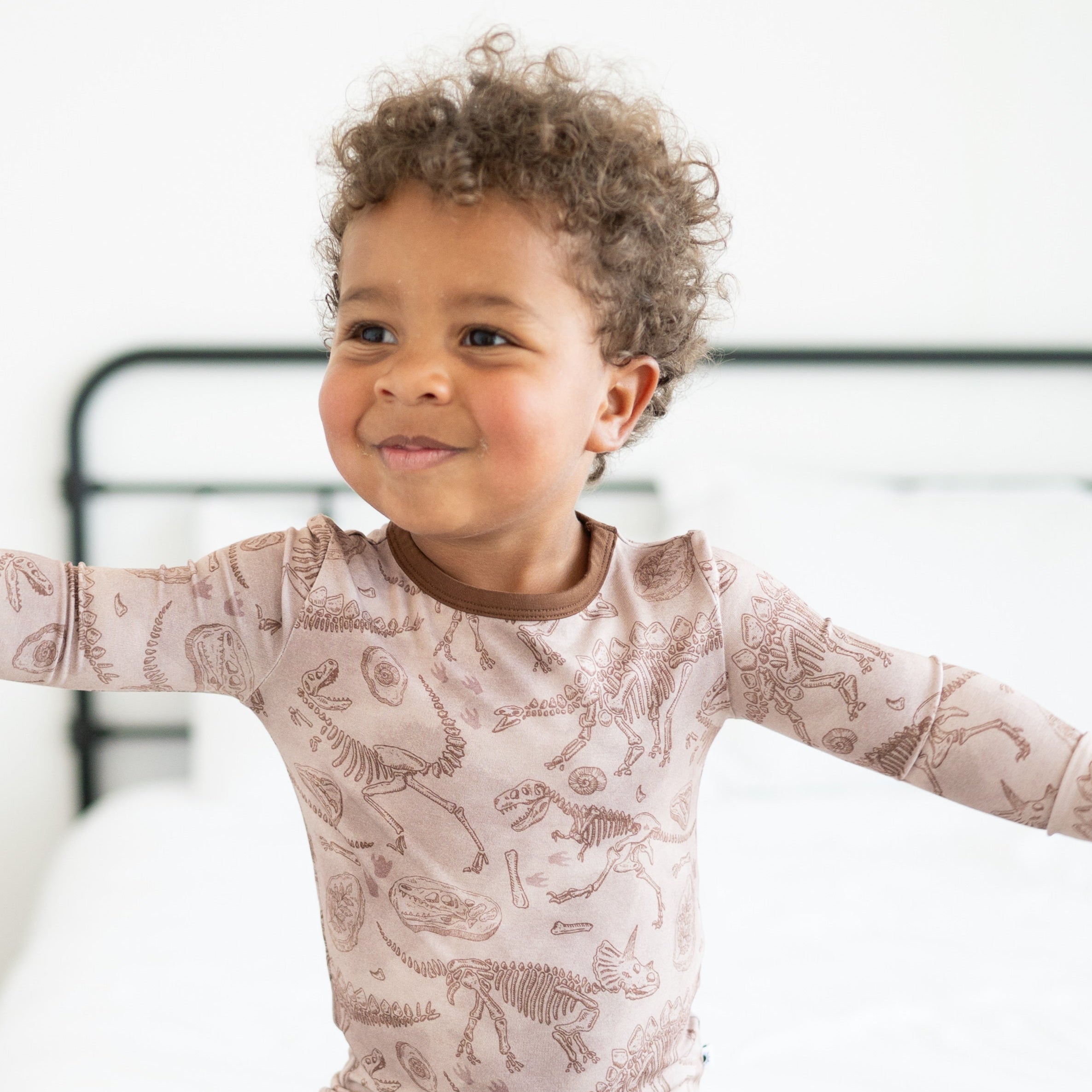 A young child wears a long-sleeved pajama set with a fossil print.