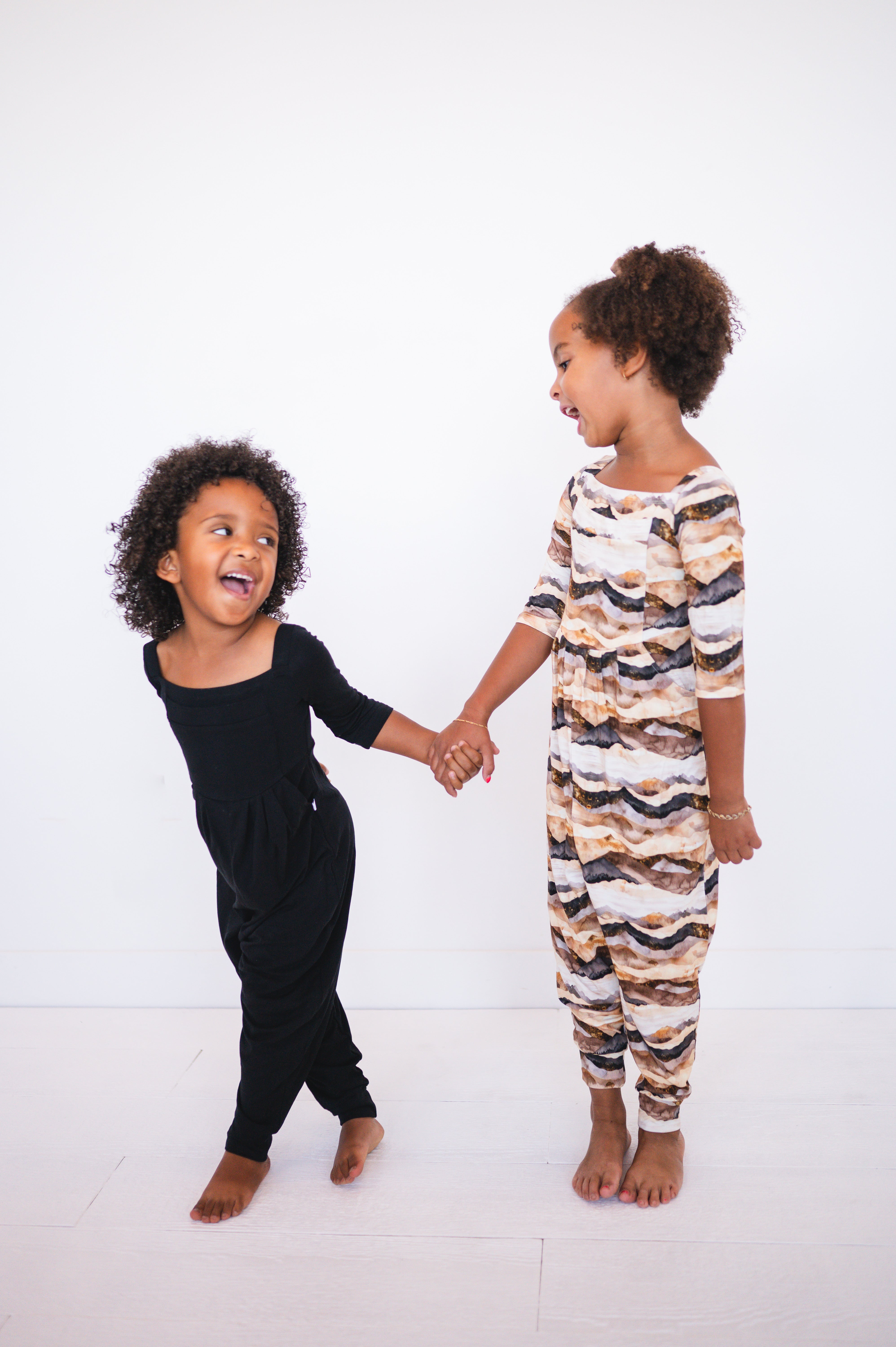 Two young girls in matching rompers holding hands.