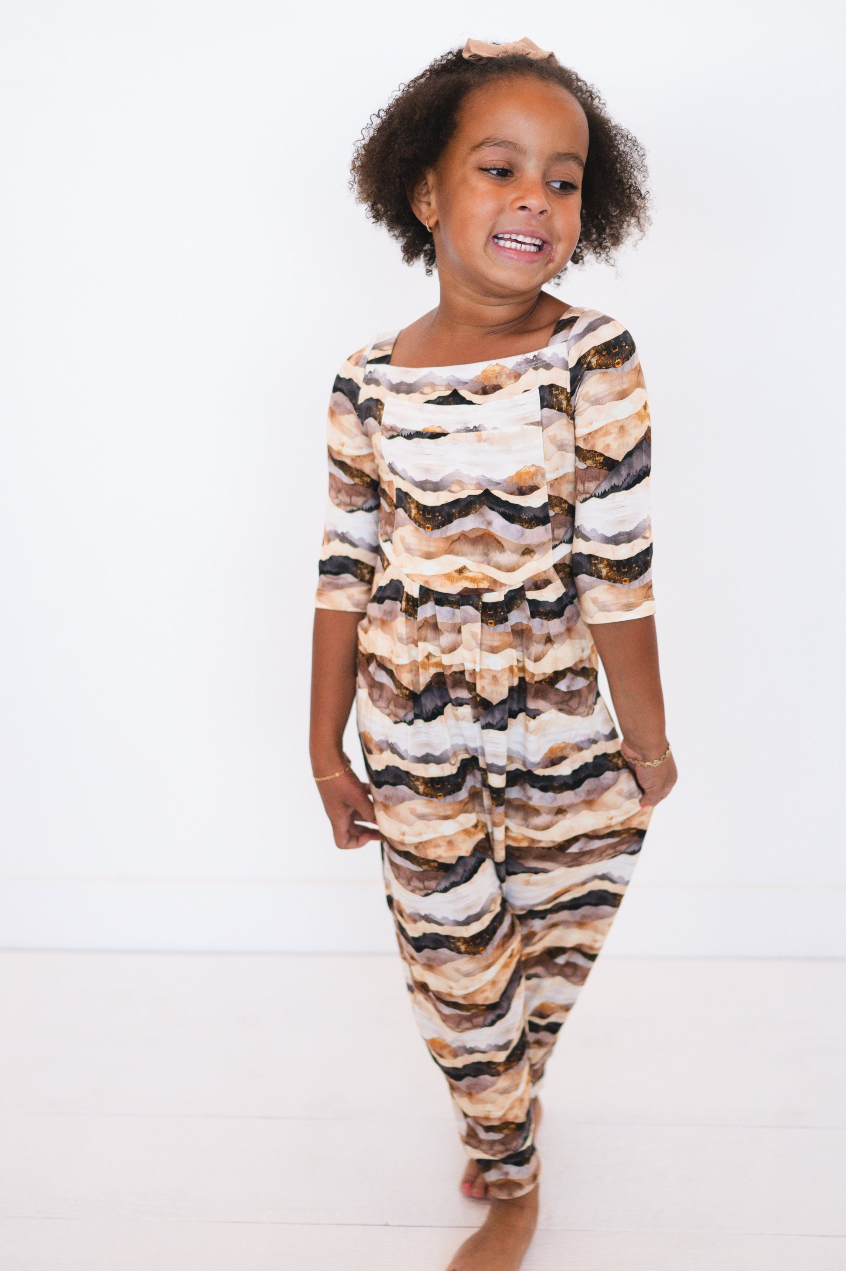 A young girl wears a long-sleeved romper with a mountain range print.