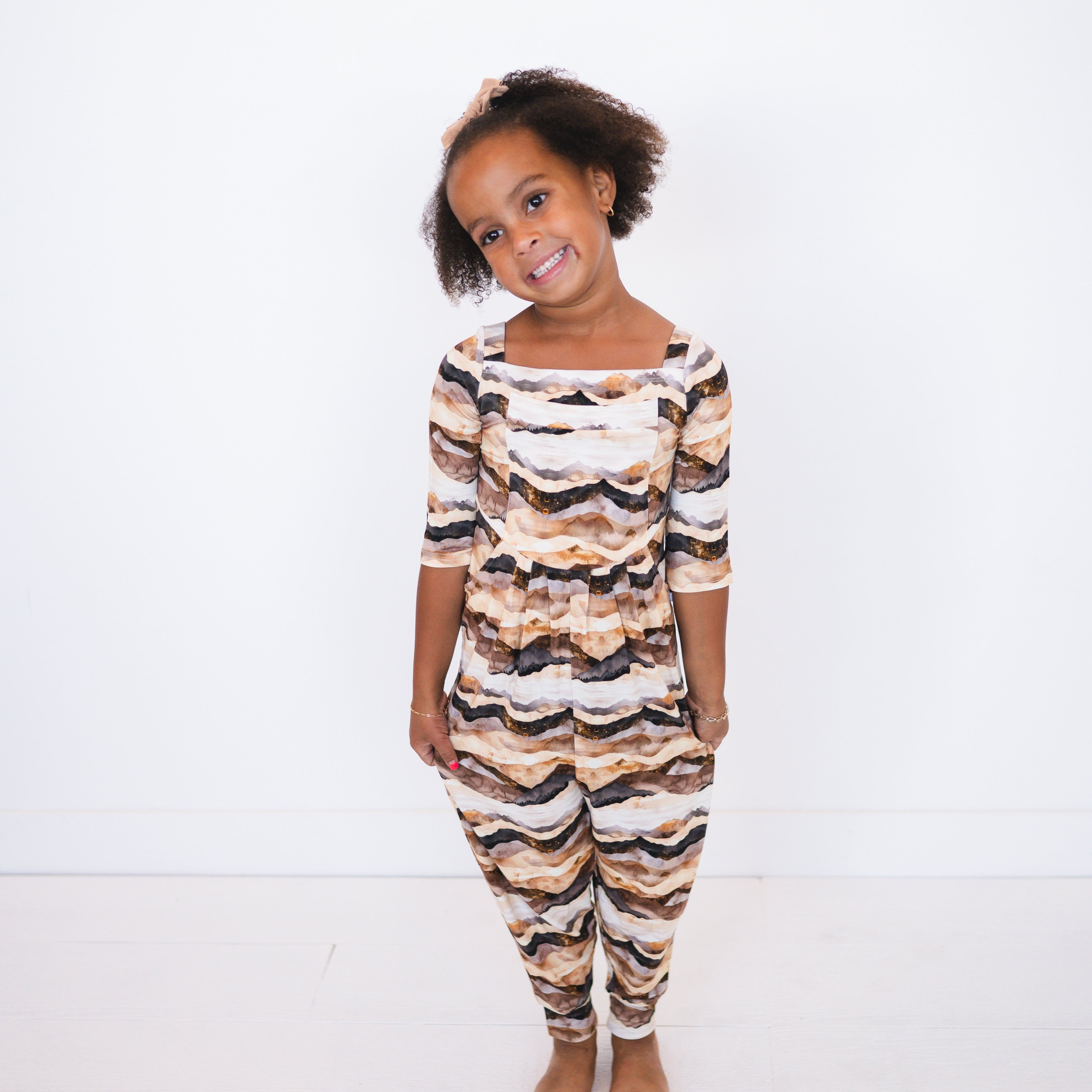 A young girl wears a brown and tan mountain range print romper.