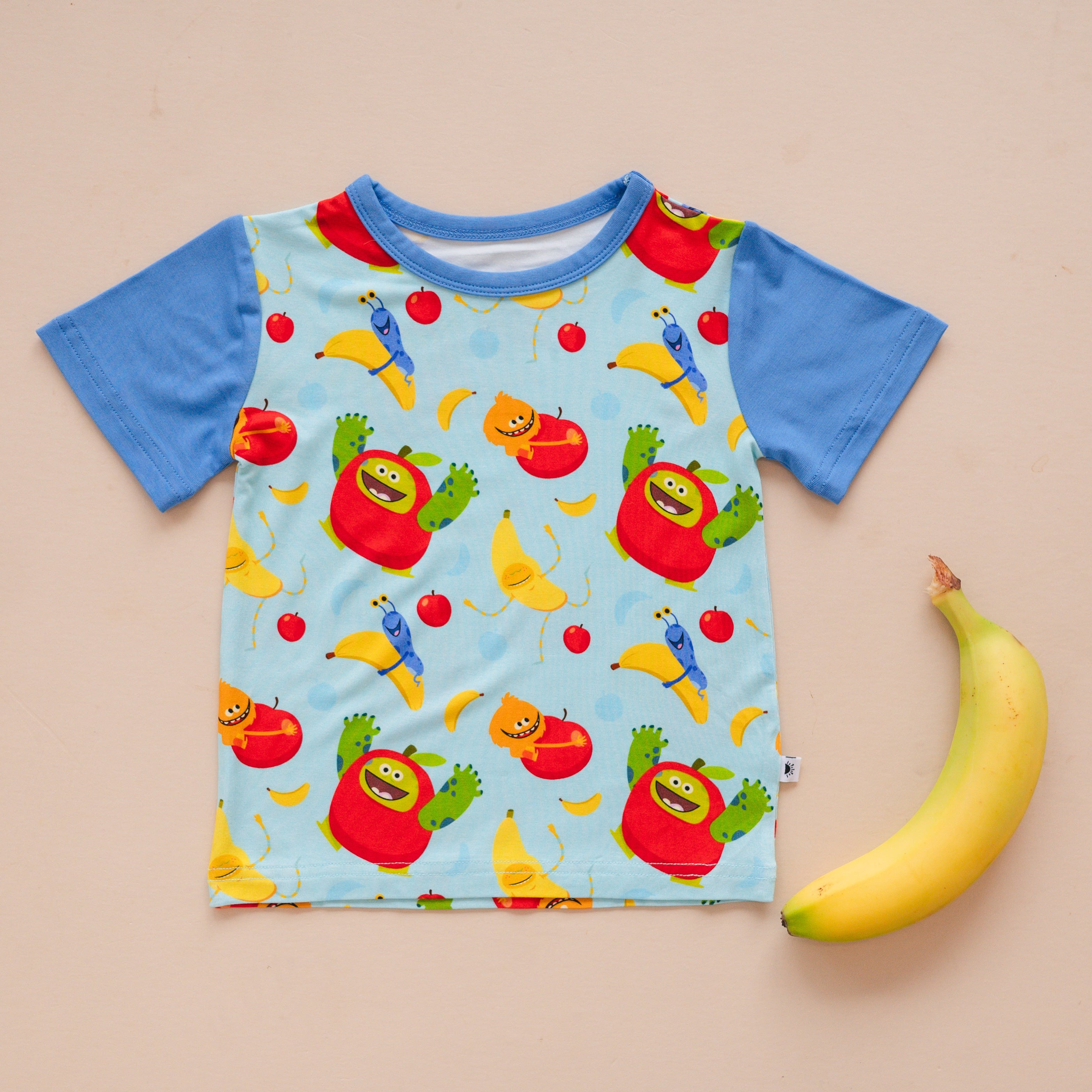 T-shirt with a light blue background featuring cartoon apples and bananas.