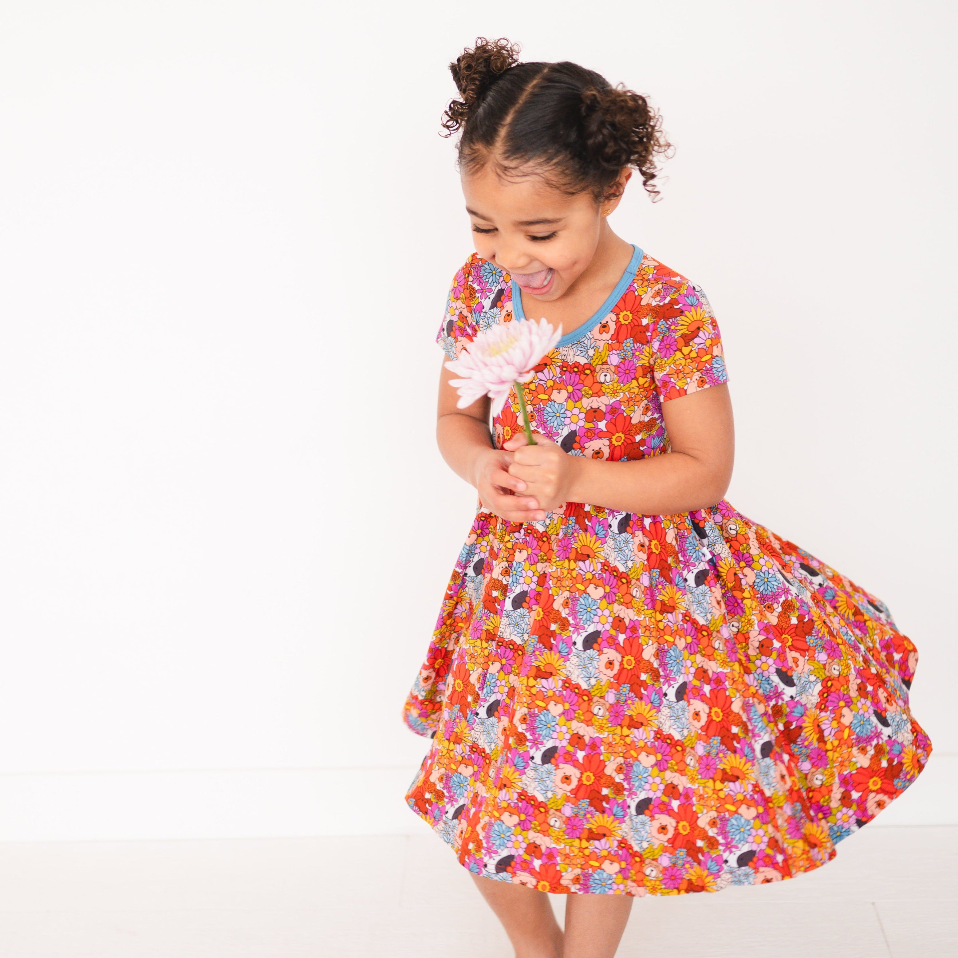A young girl in a colorful floral dress holds a pink flower.