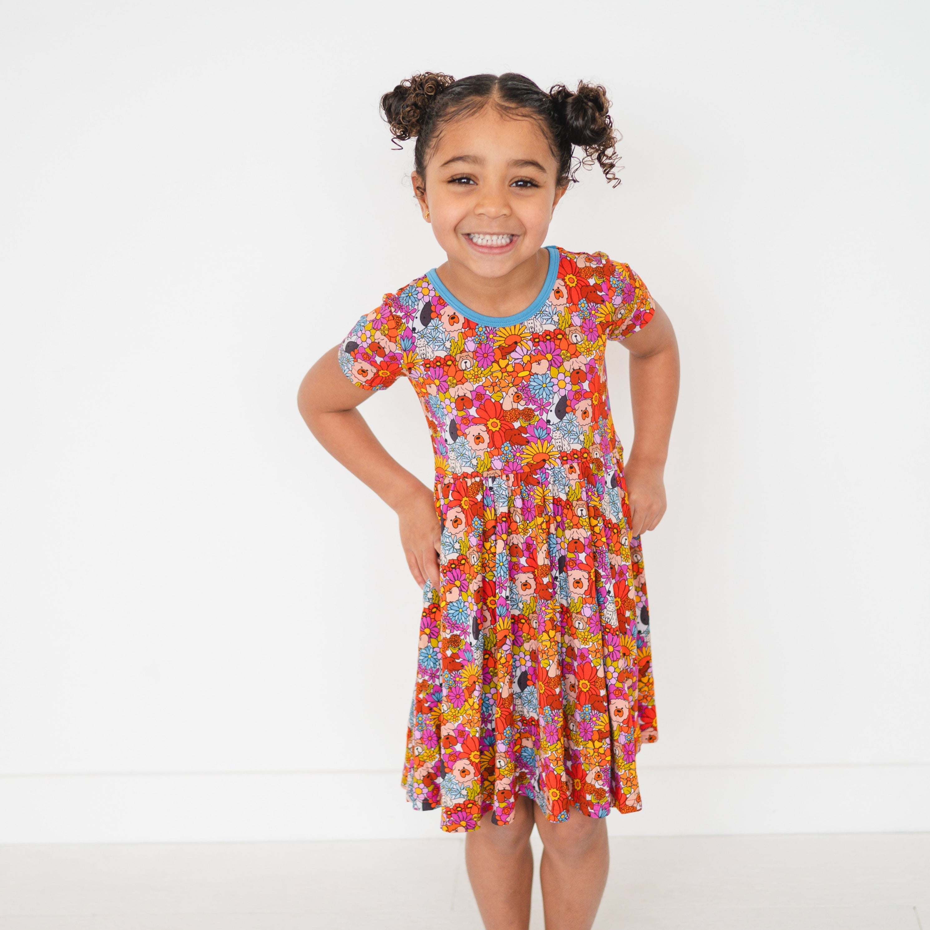 A young girl smiles in a colorful floral and dog print dress.