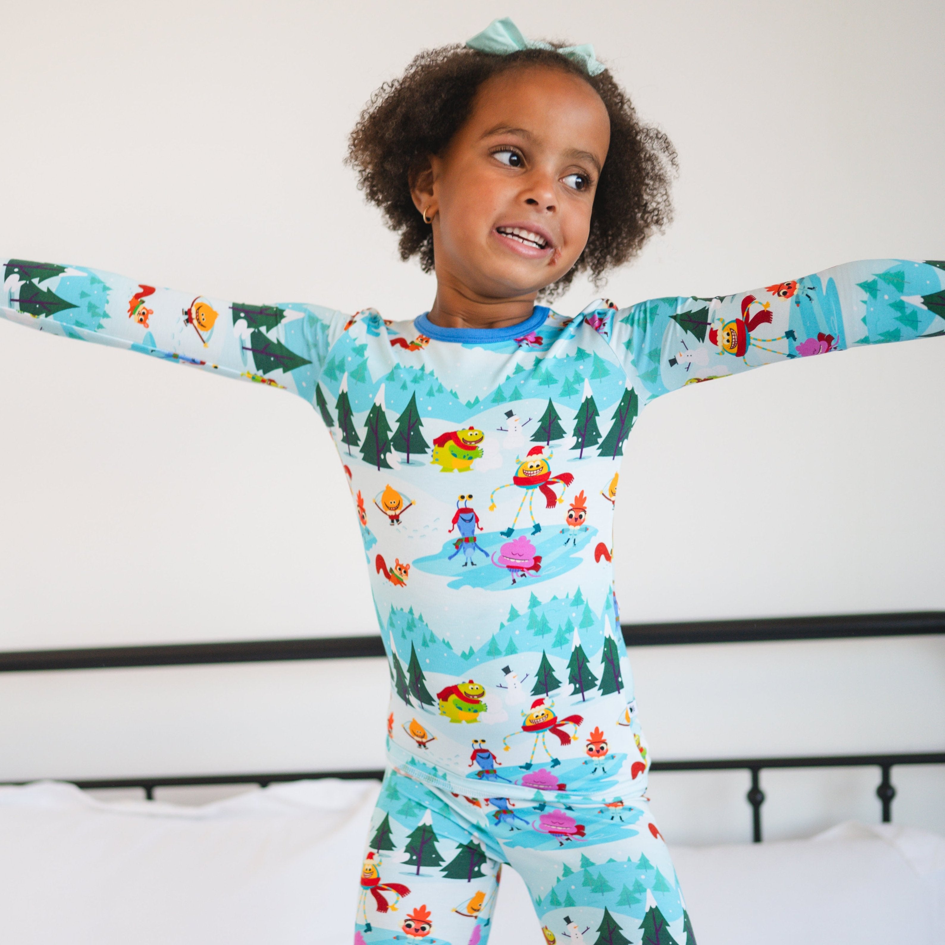 A young girl wears a light blue pajama set with a winter scene and cartoon characters.