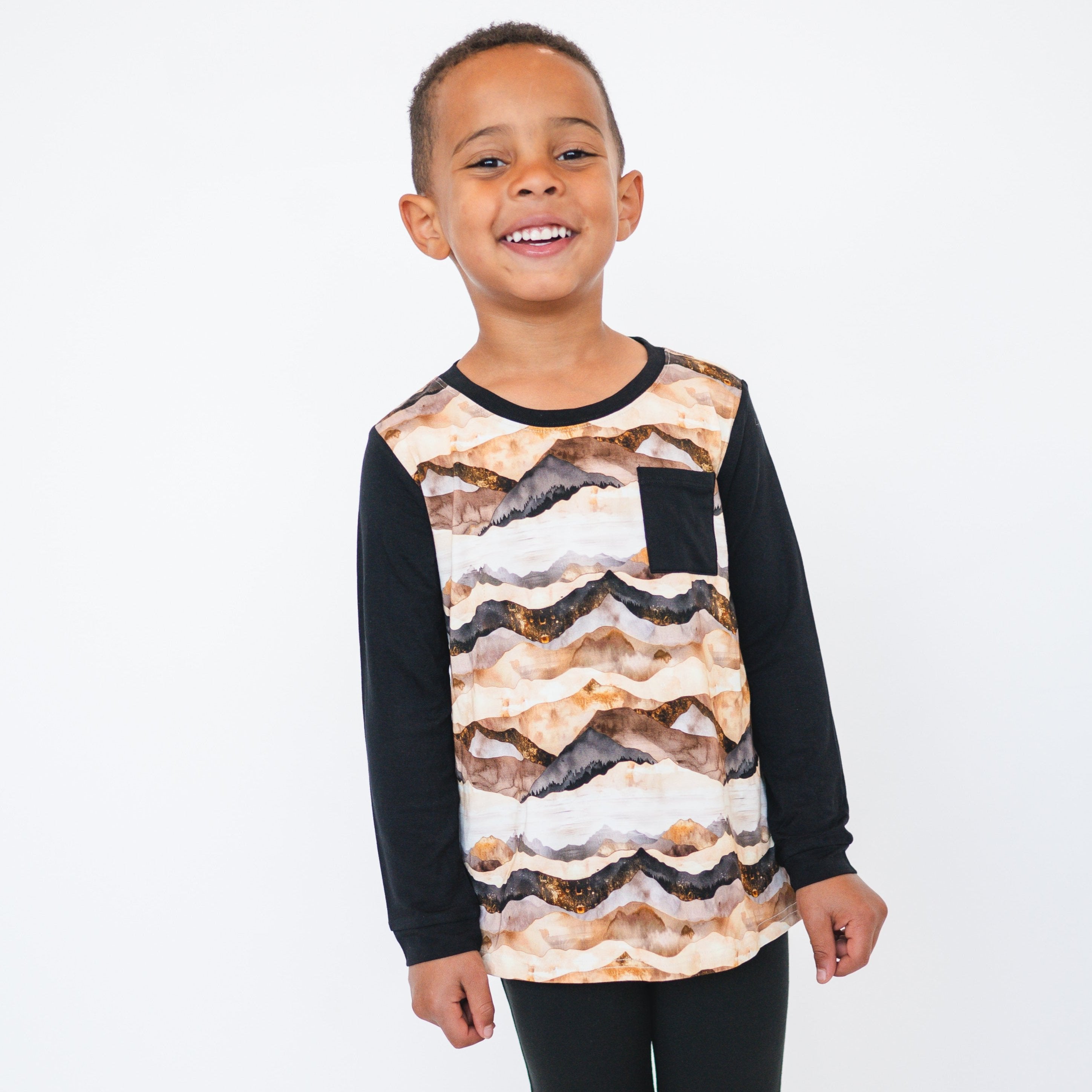 Boy wearing a long-sleeved shirt with a mountain range print and a black pocket.