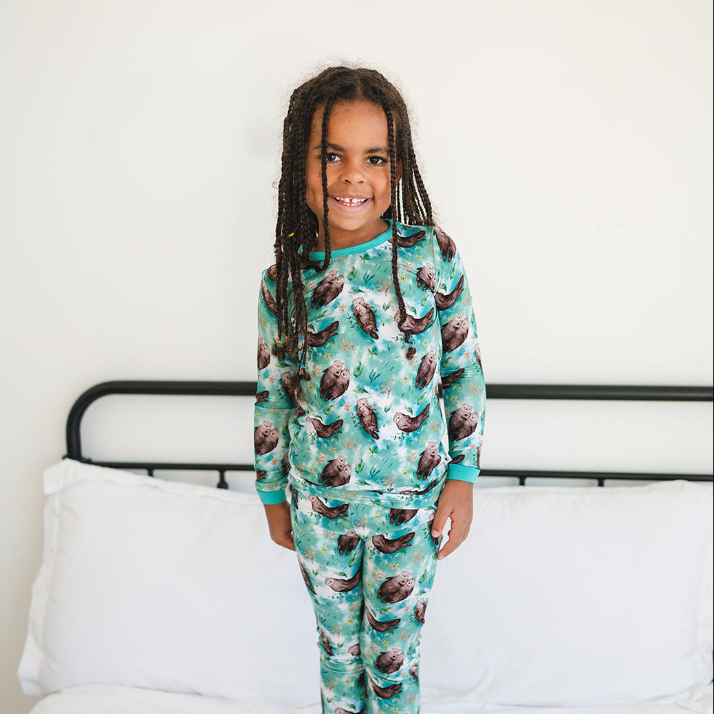 A young child smiles while wearing a long-sleeved pajama set with an otter print.