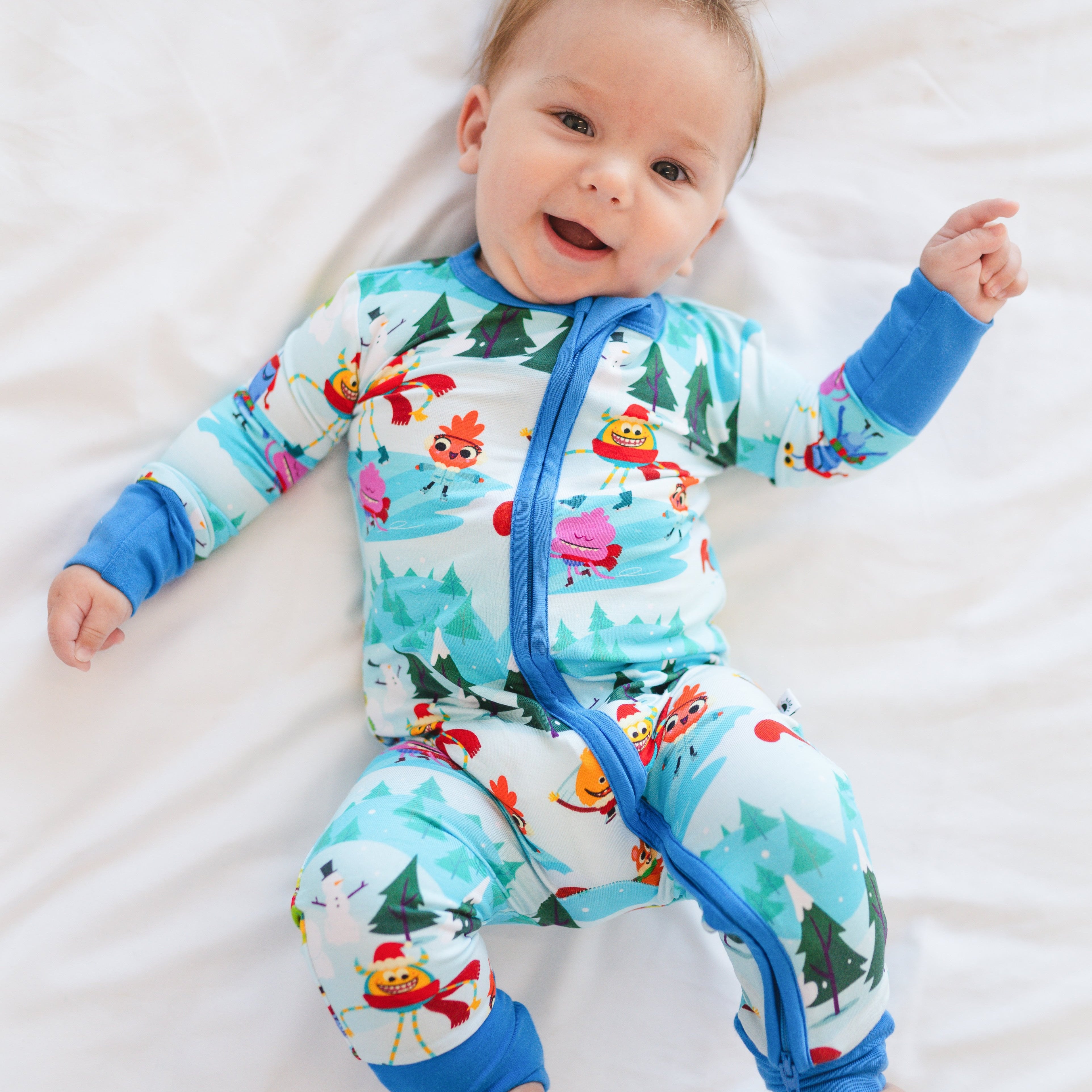 A baby wearing a light blue bamboo zip pajama set with a winter monster print.
